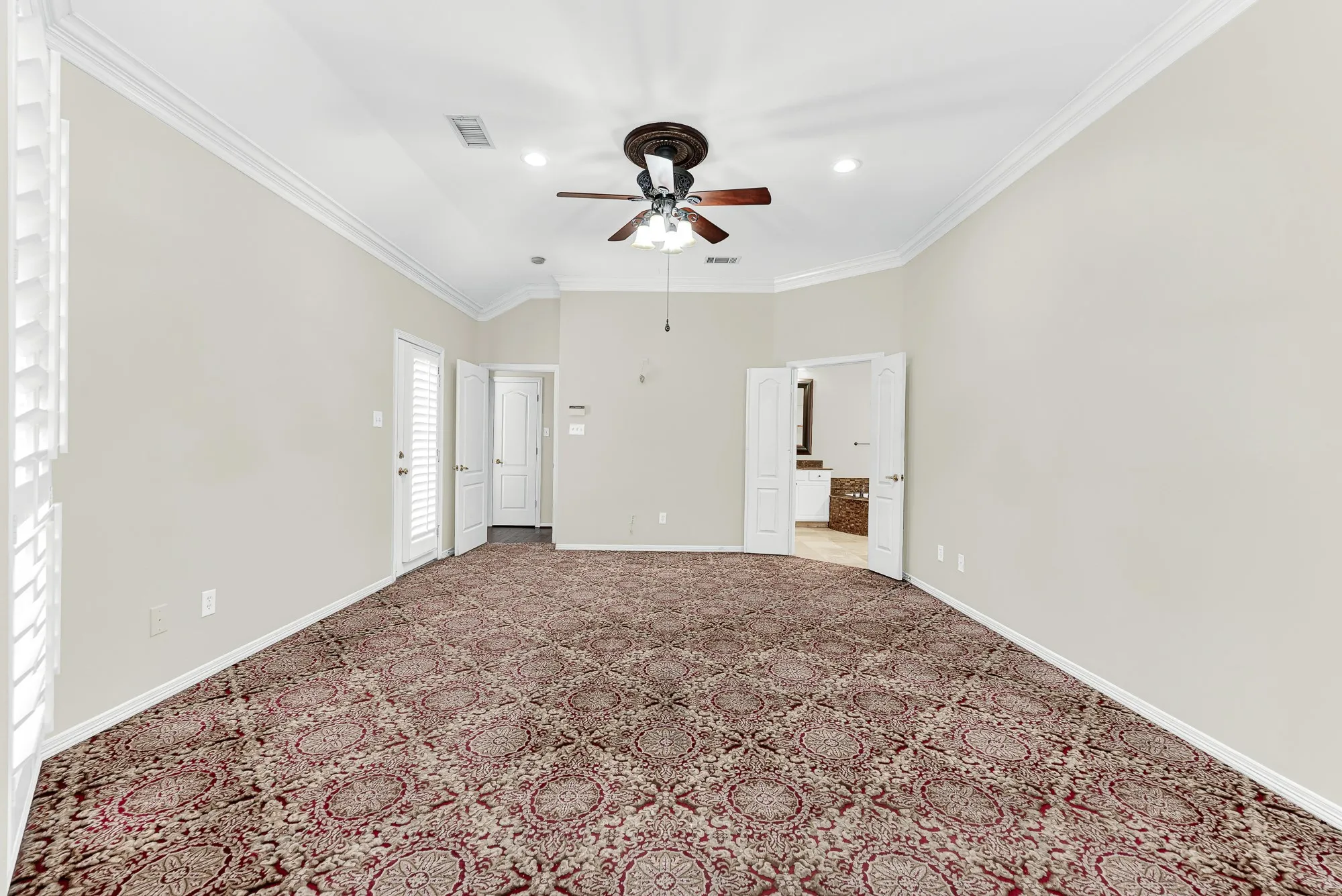 Looking back across the room reveals double doors into the primary bathroom, clean neutral walls, and plenty of space for a full bedroom set. It offers a warm, quiet retreat designed for relaxed evenings and effortless daily routines.