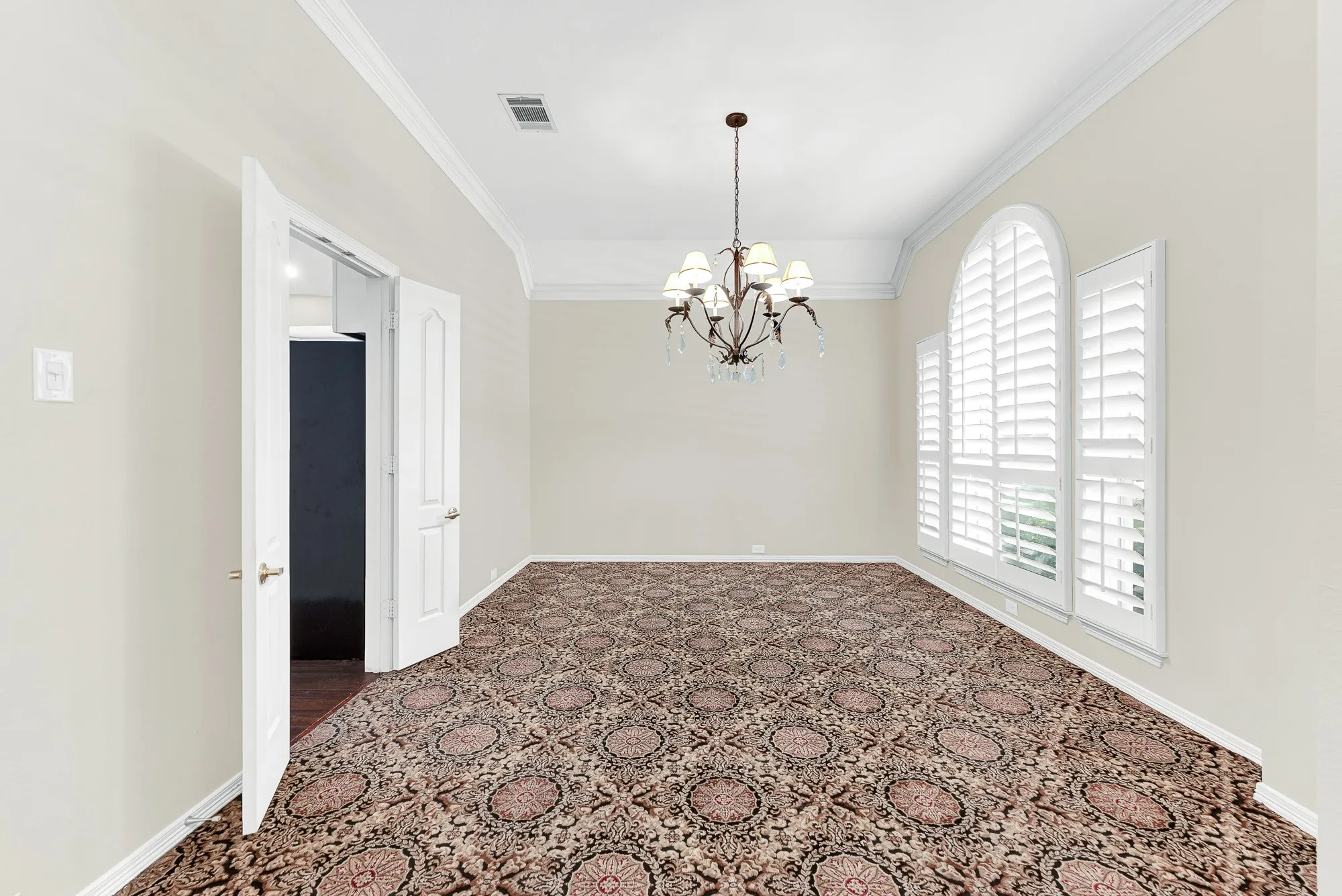 An elegant chandelier, arched window with plantation shutters, and patterned carpet frame this formal dining room, complete with direct kitchen access. It provides the perfect backdrop for hosting holiday feasts or gathering loved ones for unforgettable dinners