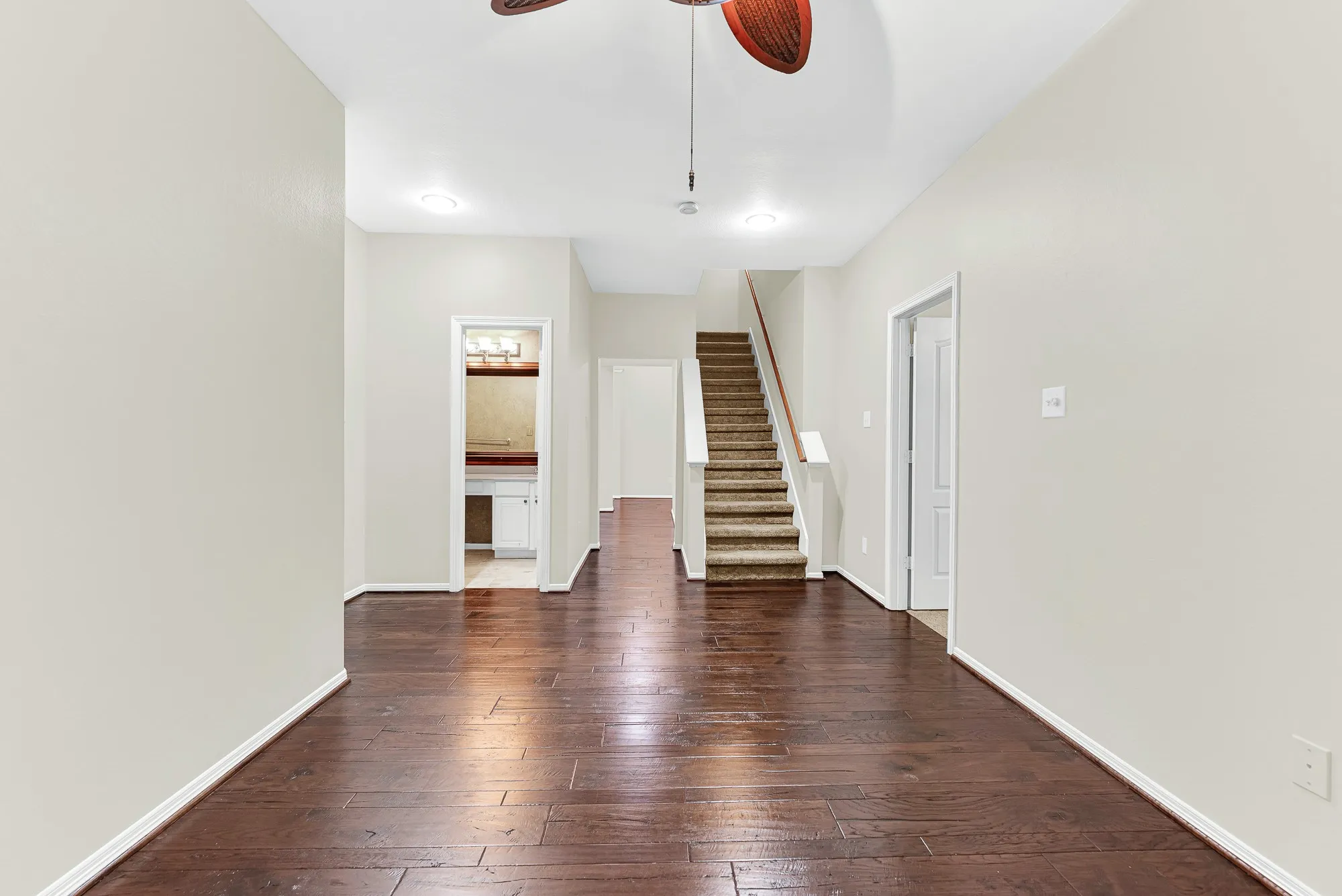 Looking across the warm wood floors, this reverse view reveals the adjoining full bathroom, staircase access, and fluid connection to the rest of the main level. It creates an inviting layout that makes entertaining, hosting sleepovers, or moving throughout the home feel completely effortless.
