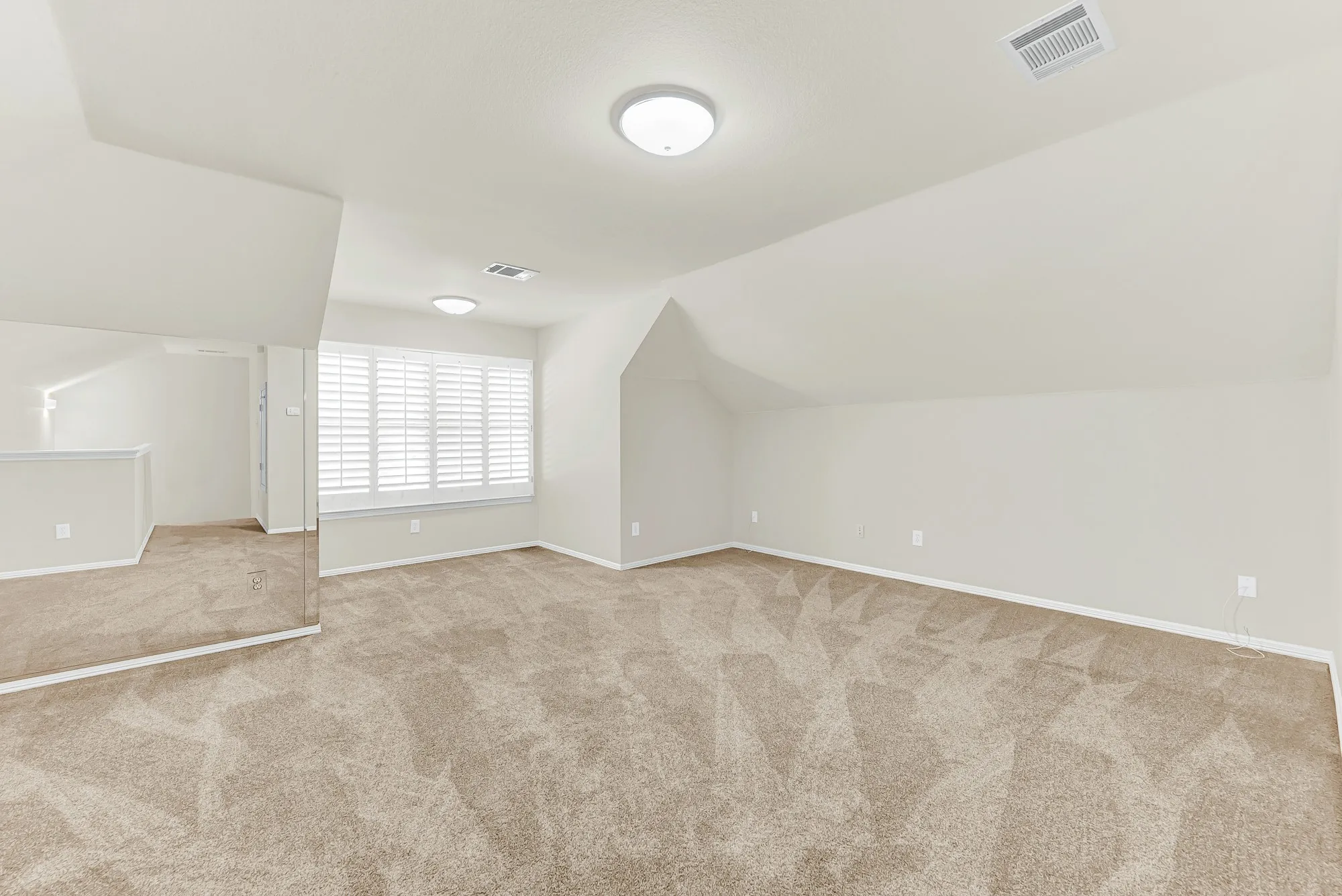 This versatile upper-level bonus room features soft carpeting, warm neutral paint, a mirrored wall section, and a bright window framed by plantation shutters. It offers an ideal setup for a quiet home workout space, private office, or cozy media lounge away from main living areas.