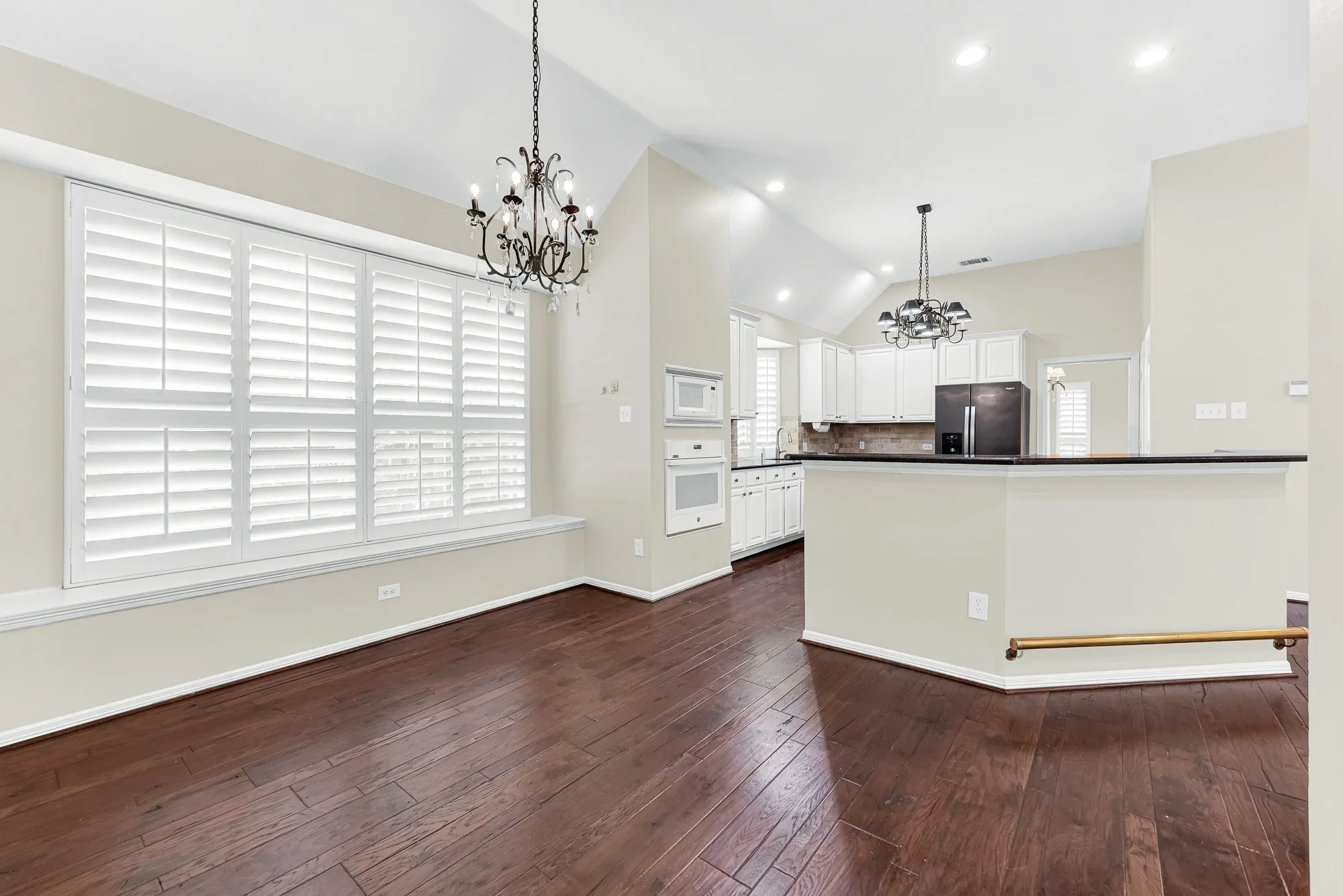 Framed by vaulted ceilings and dual chandeliers, this shot shows the easy transition from the window-lit dining area to the kitchen bar. It provides a versatile space where family dinners can naturally extend into casual evening conversations.