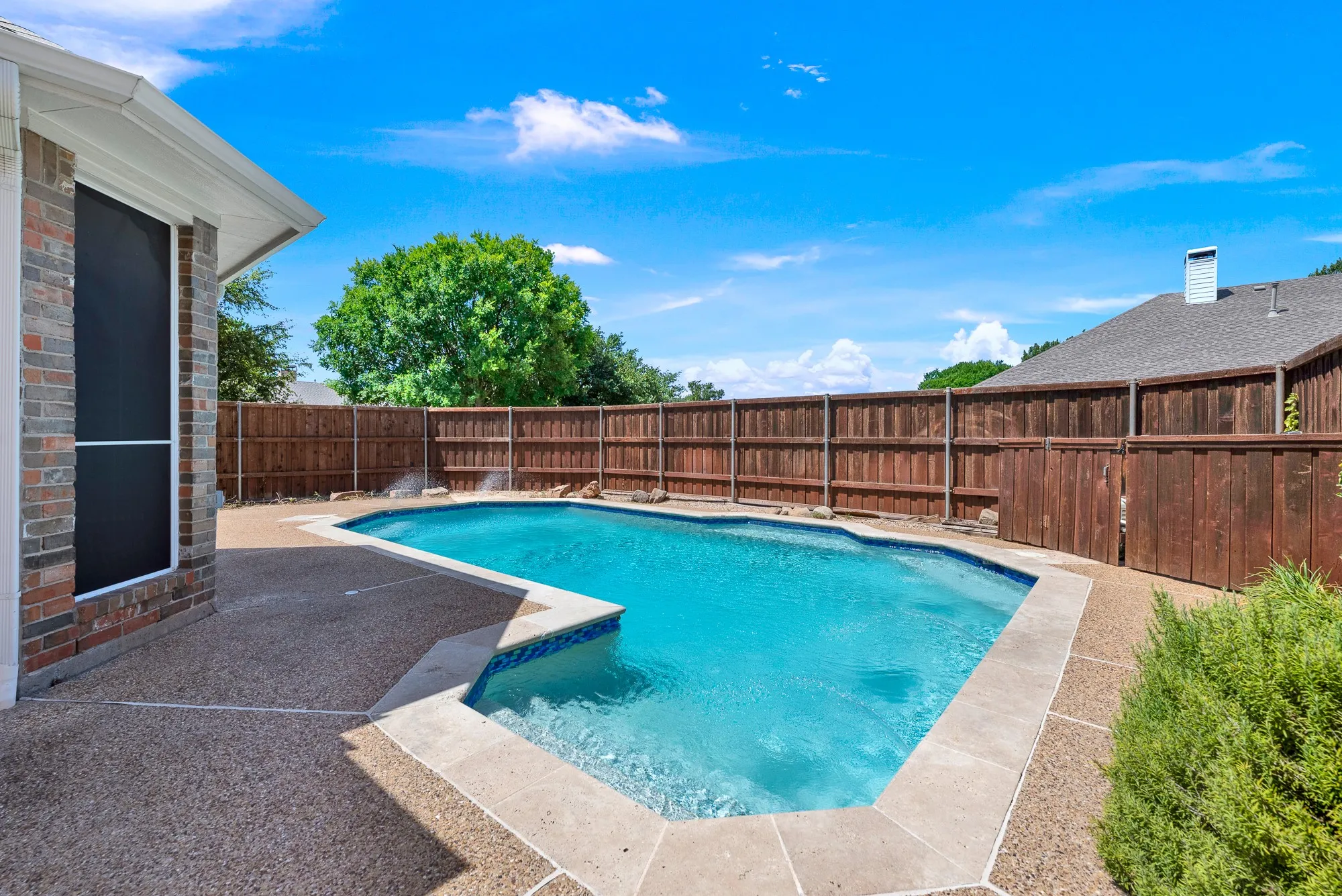 A sparkling blue pool bordered by coping and cool-tone patio decking forms a private backyard oasis enclosed by high wooden privacy fencing. It offers a refreshing escape where you can cool off during warm summer afternoons or lounge poolside in complete privacy.