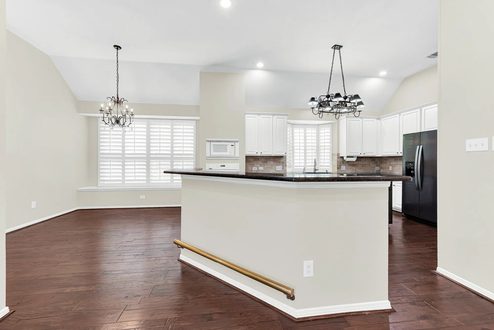 A raised breakfast bar with dark granite counters sets the stage for this open kitchen, anchored by double chandeliers and high vaulted ceilings. It creates an easy, inviting flow where guests can gather for drinks while you finish prepping dinner.