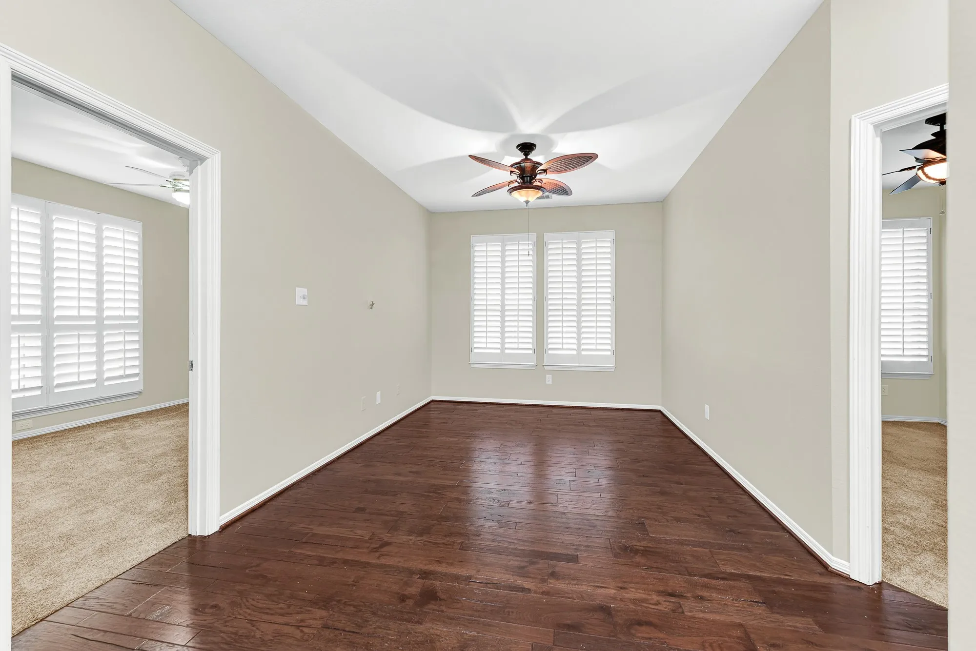 Rich hardwood flooring grounds this central first-floor game room, framed by plantation-shuttered windows, a tropical-style ceiling fan, and direct doorways to both secondary bedrooms. It offers a convenient, shared space where kids or guests can relax, study, or hang out right near their rooms.