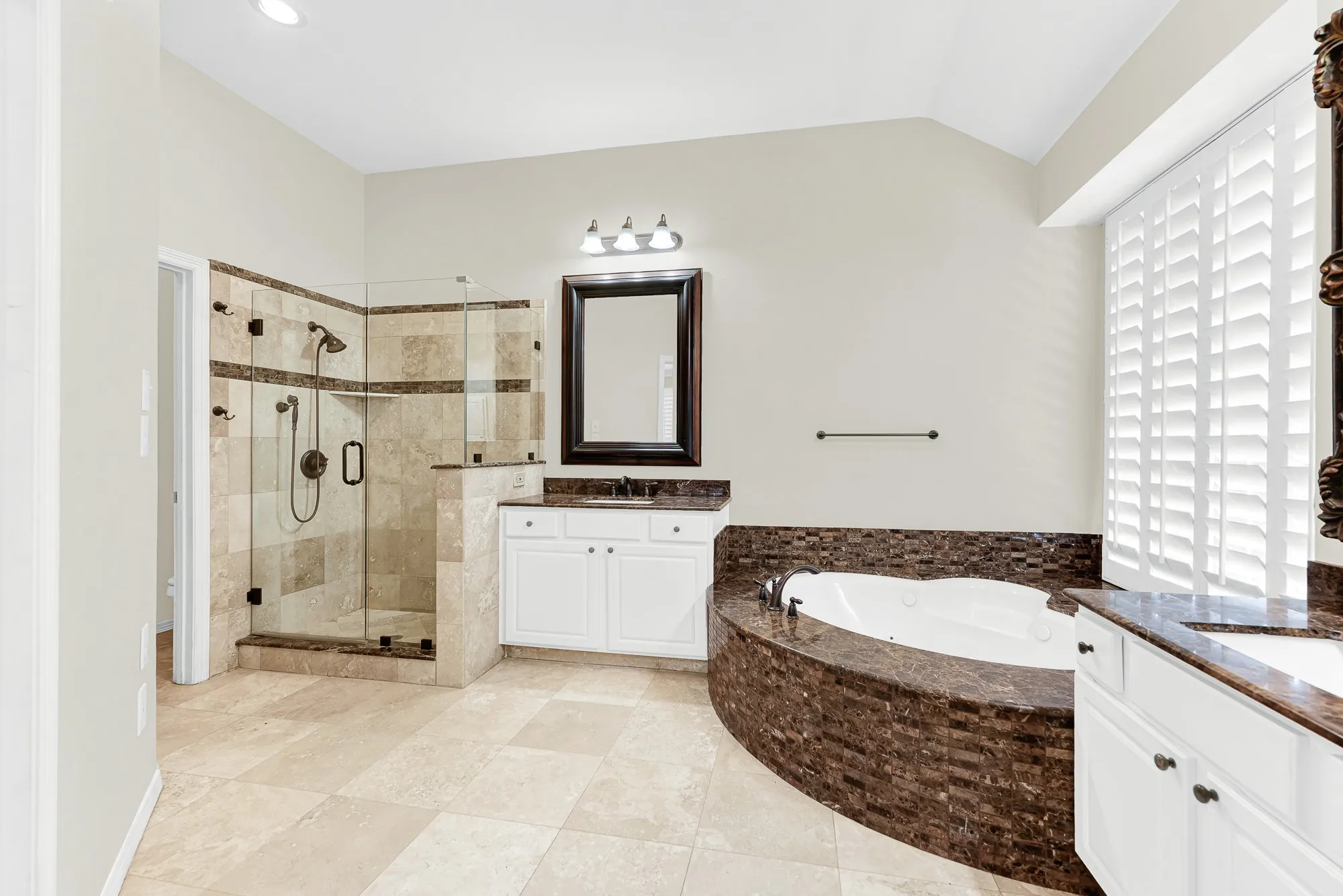This angle highlights a seamless glass-enclosed walk-in shower lined with travertine tile, positioned right beside the deep soaking tub and vanity area. You will love having a bright, invigorating space to quickly refresh every morning before taking on the day.