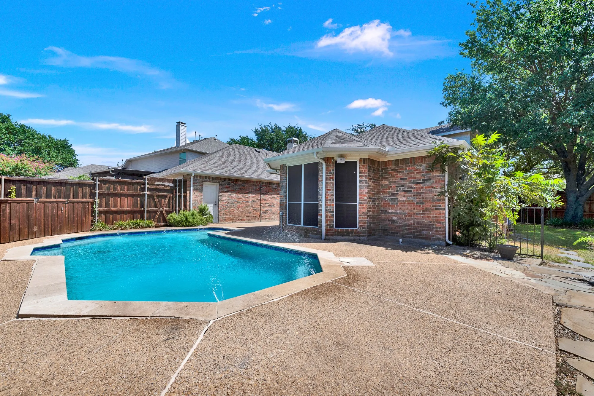 Looking across the aggregate patio deck highlights the pool layout alongside the flagstone pathway leading toward the side yard. You will love having plenty of open patio space for lounging chairs, outdoor dining setups, and lively summer gatherings.