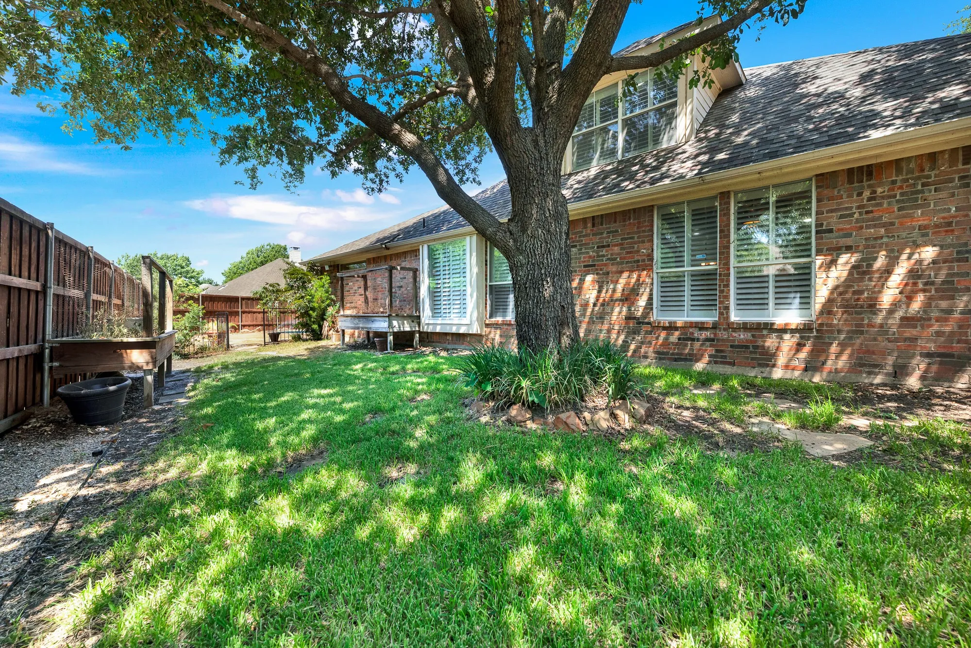 Shaded by a grand oak tree, this lush grassy side yard features raised garden beds along a dark wood privacy fence. It offers a peaceful outdoor retreat where you can relax in the shade, tend to fresh plants, or enjoy quiet weekend mornings.