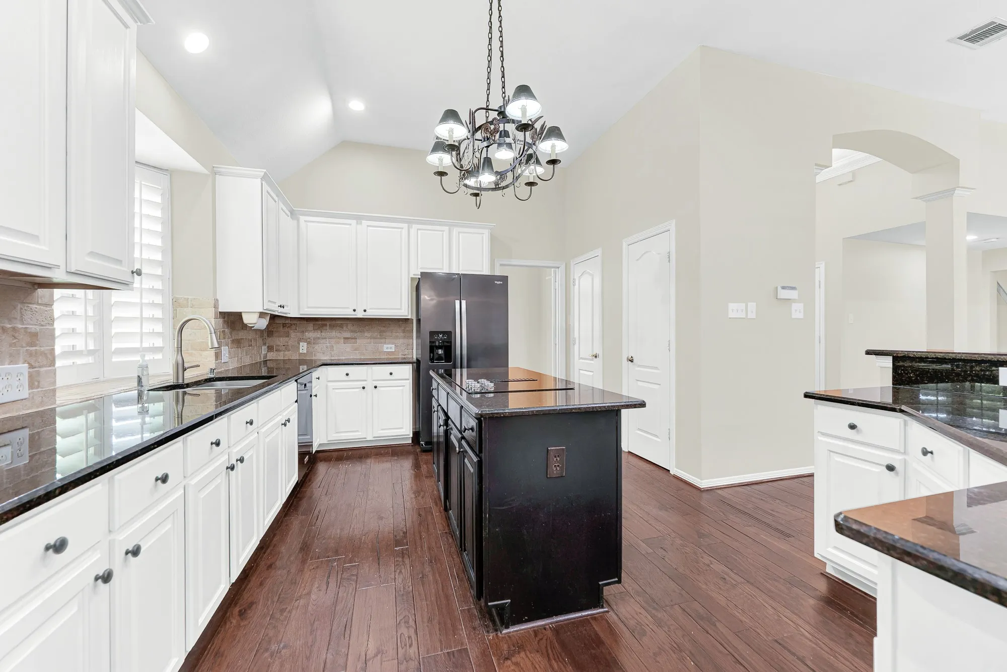 A wide perspective down the main aisle highlights the contrast between the dark island, white surround cabinets, and the built-in double ovens. It gives home chefs plenty of room to cook together without ever feeling crowded.
