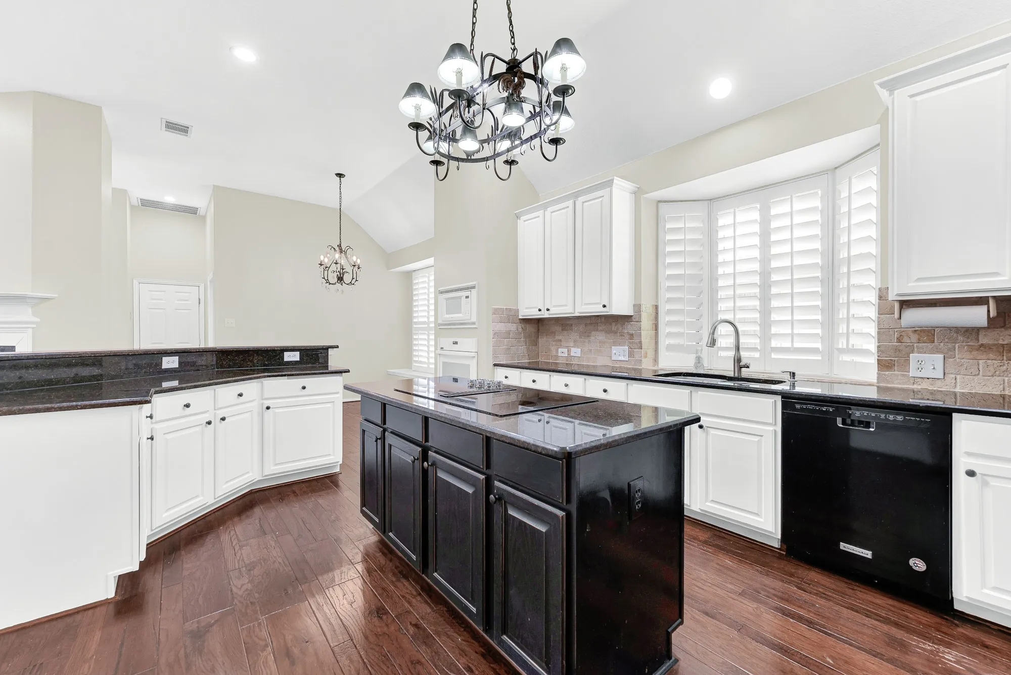 Looking across the dark granite island, this angle showcases the bright bay window over the sink, gleaming dark hardwood floors, and extensive counter space. It offers a warm setting to enjoy morning prep while daylight streams in through the shutters.