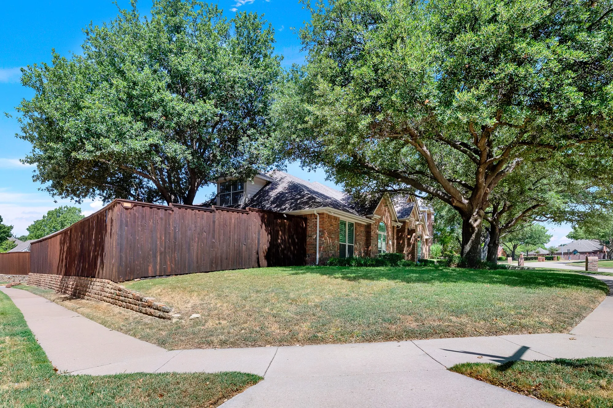 A sweeping view of the side lawn showcases a impressive shade tree framing the back brick elevation and private garden area. This extra green space on the corner lot gives you room to relax outdoors, tend to your garden, or simply enjoy quiet mornings under the trees.