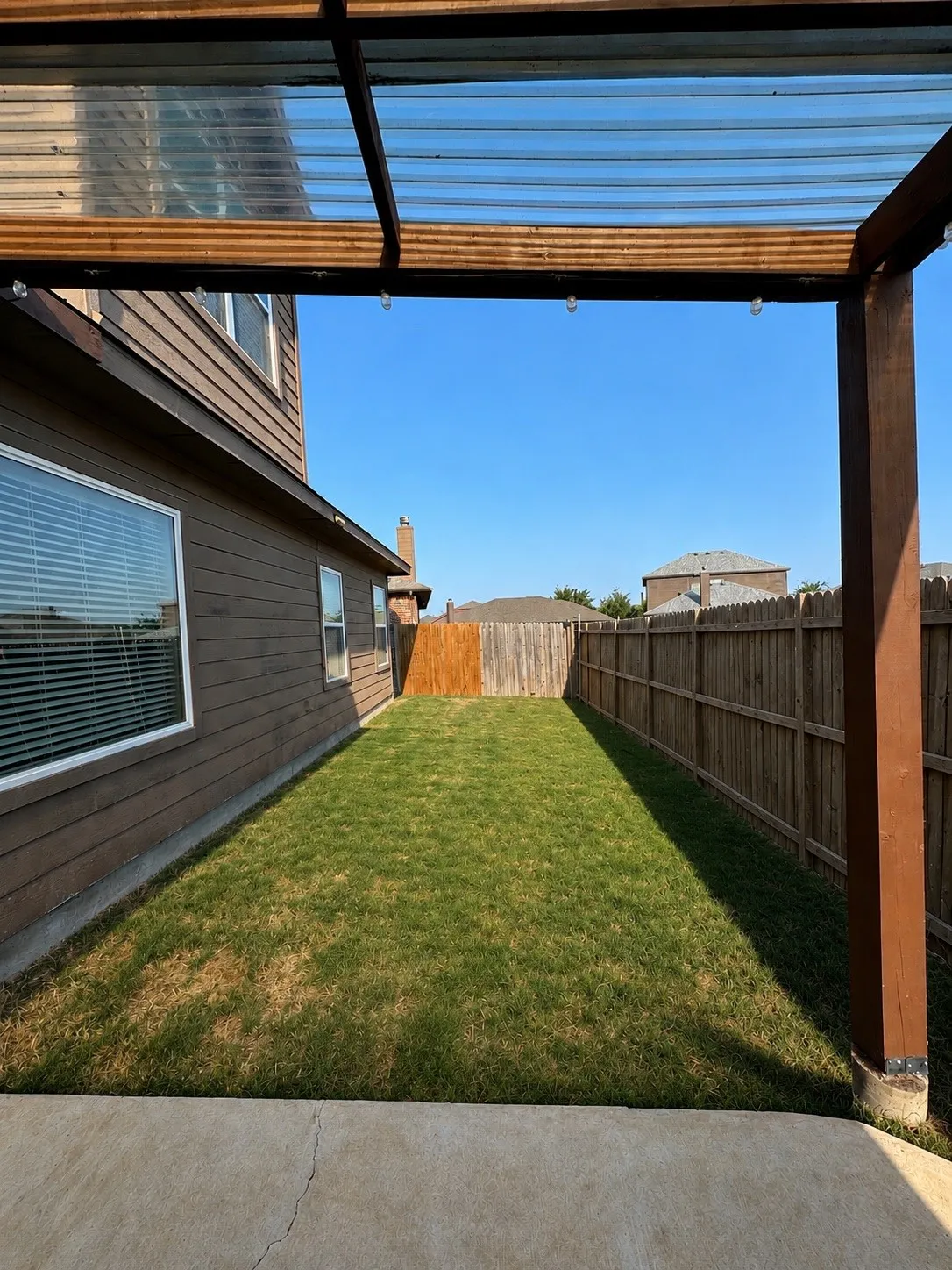 Covered patio area with concrete flooring, wood-framed translucent roof, and string lighting