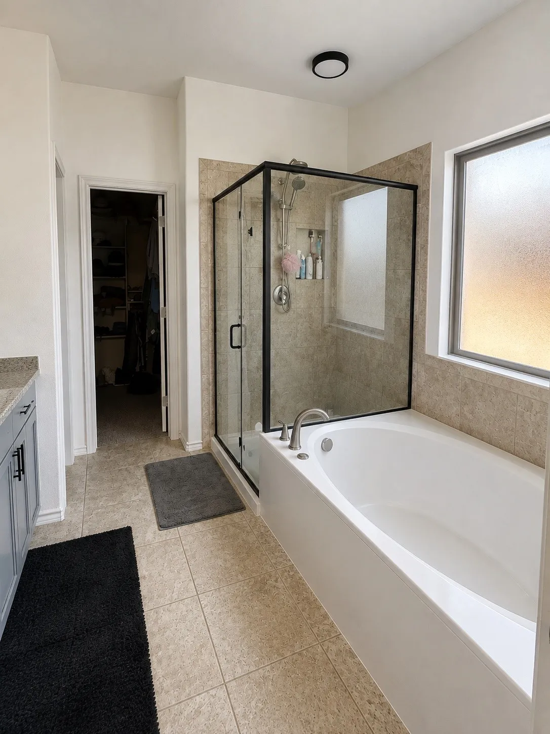 Enclosed glass-front shower with black framing, tiled shower surround, recessed built-in tub, and tiled flooring