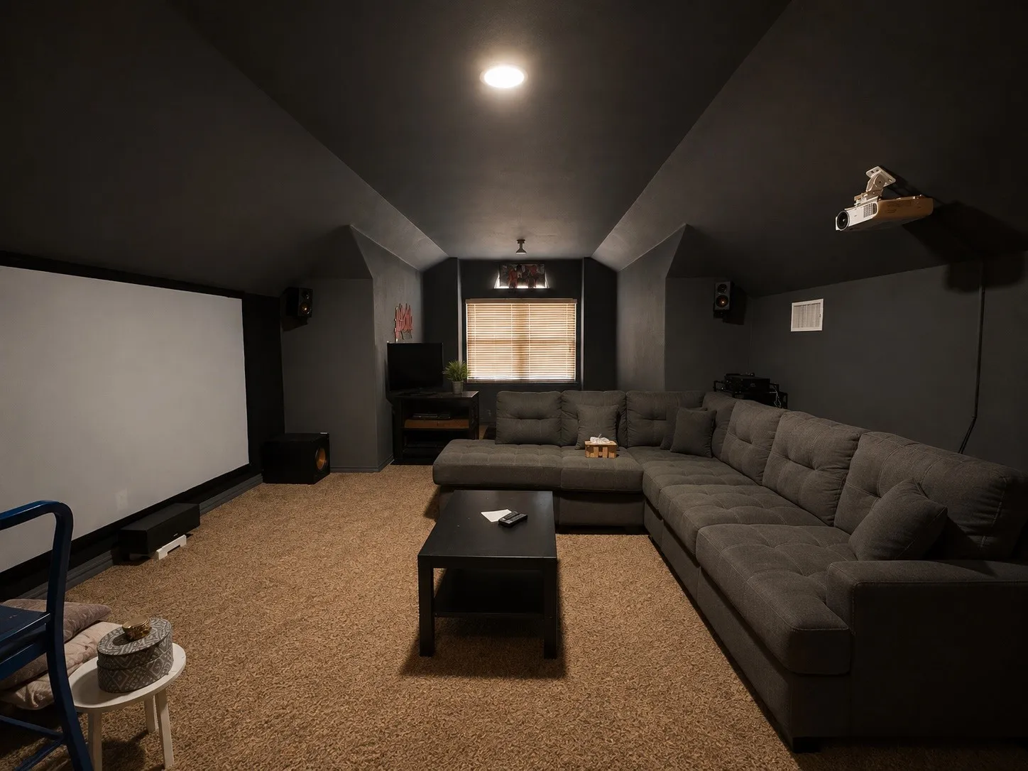 Carpeted media room with a projector screen, ceiling-mounted projector, recessed lighting, and a window with blinds
