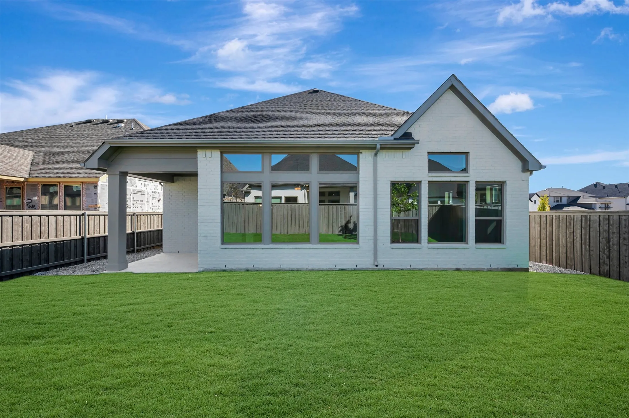 Expansive green lawn with a covered patio, large windows, and a white brick exterior