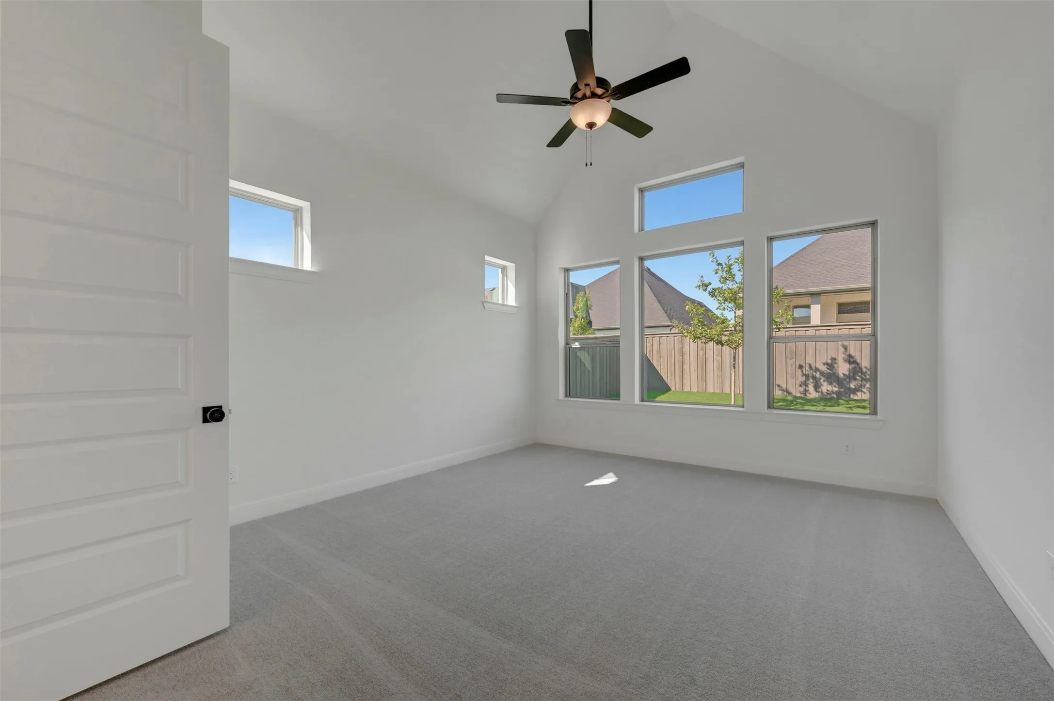 Vaulted ceiling with a ceiling fan, light-colored carpeting, multiple windows, and a paneled interior door