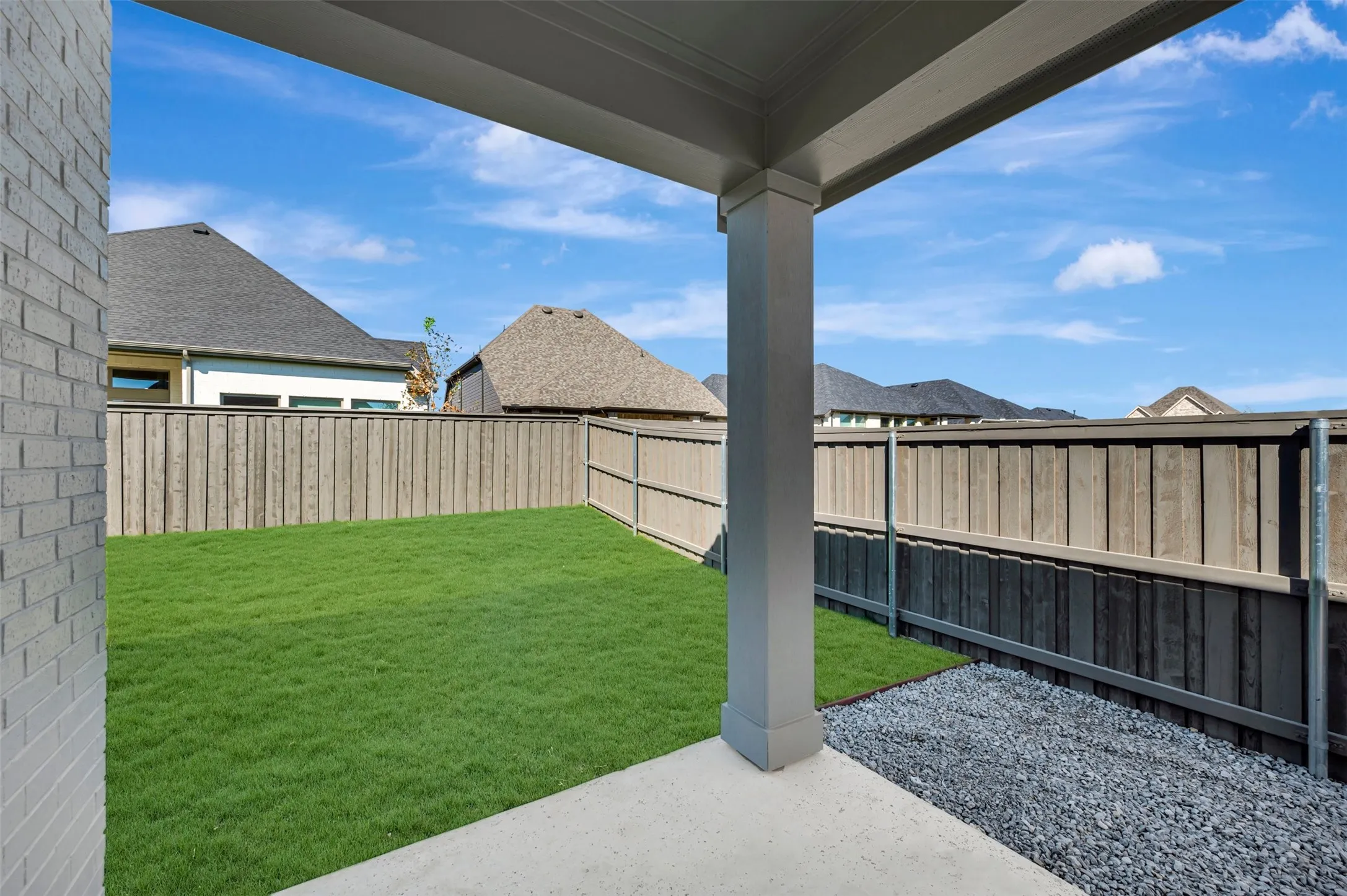 Covered concrete patio with a white brick exterior wall, leading to a lawn area and a gravel perimeter