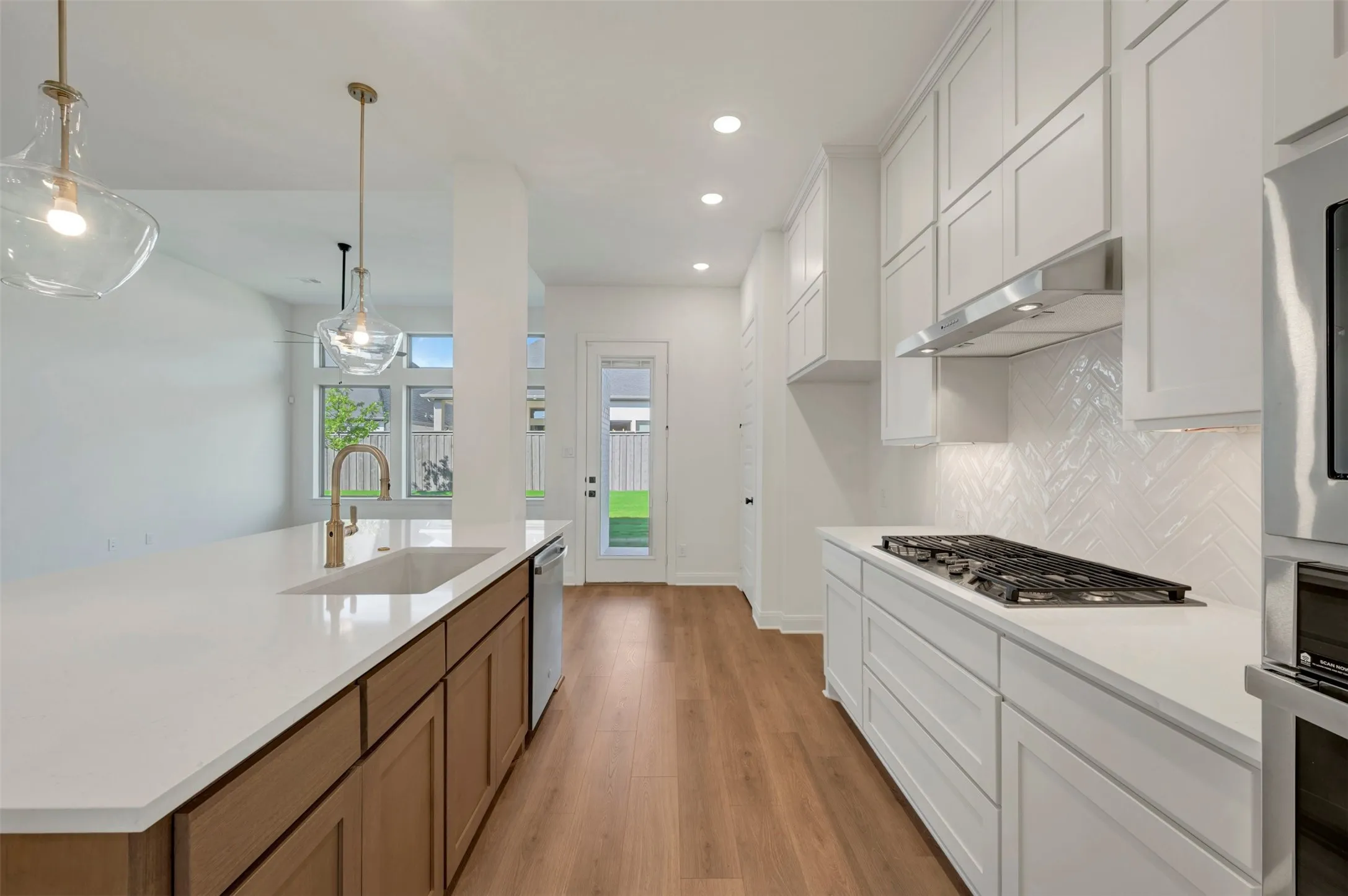 Modern kitchen featuring white shaker cabinetry, white countertops, wood-finish flooring, and a herringbone tile backsplash