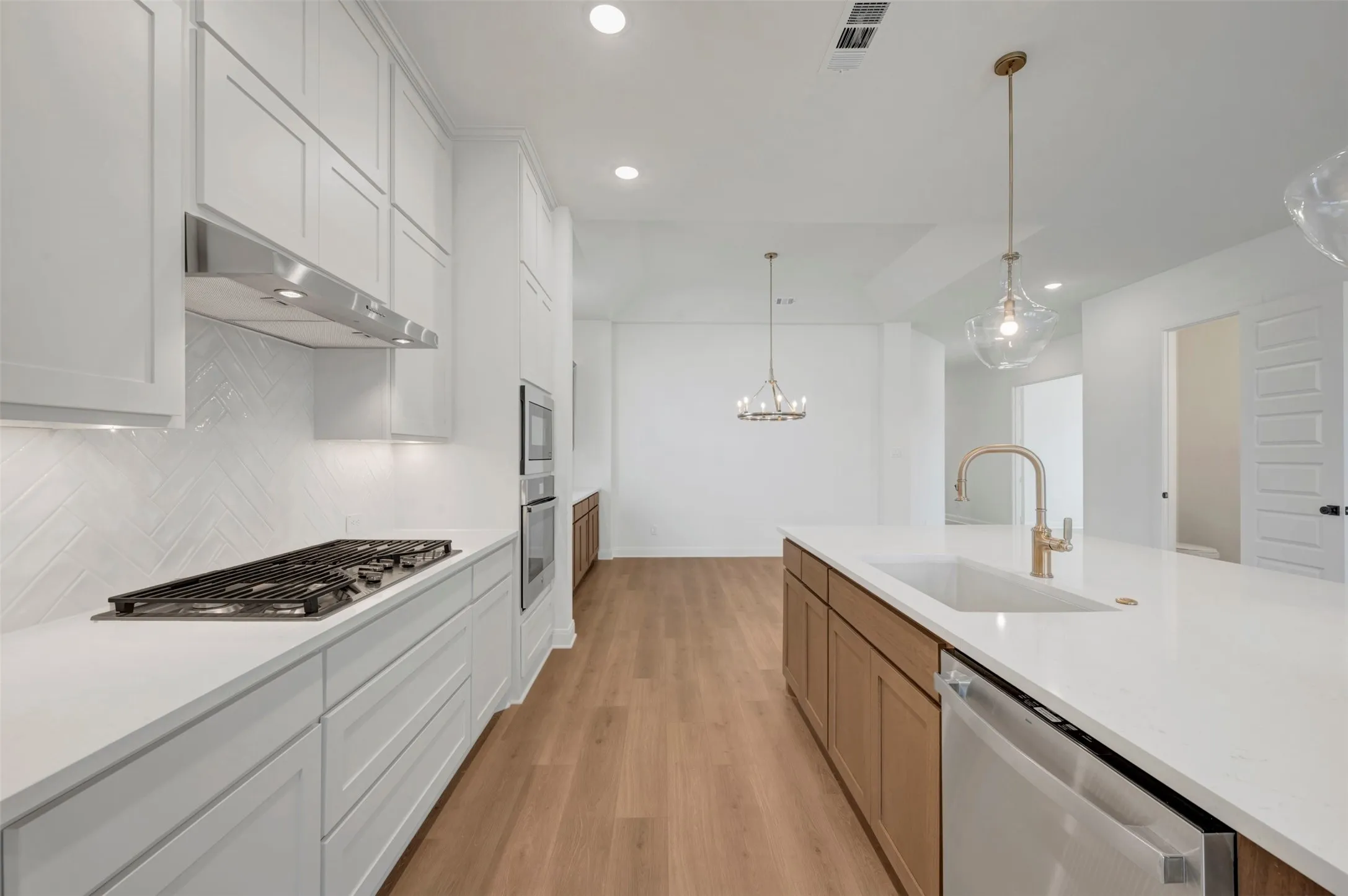 Kitchen featuring a gas range, stainless steel appliances, white cabinetry, a large center island with an undermount sink, and wood-finish flooring