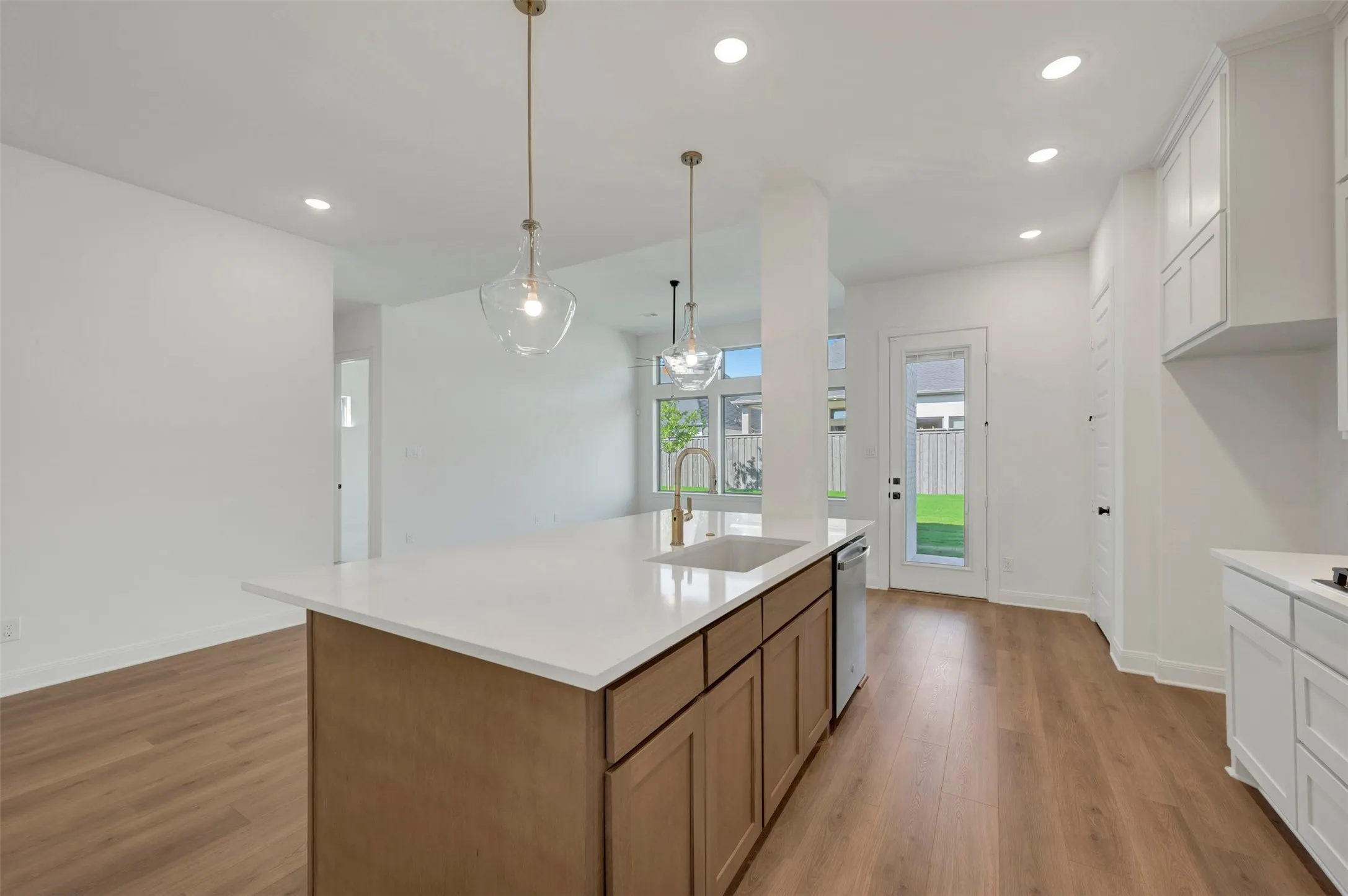 Open-concept living area featuring wood-finish flooring, a kitchen island with a light-toned countertop, pendant lighting, recessed ceiling lights, and white cabinetry