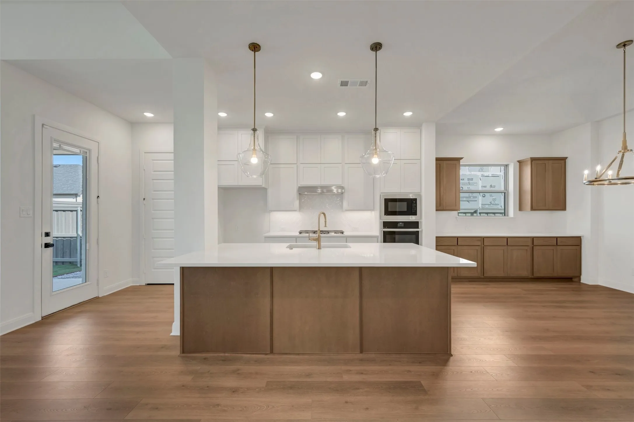 Open-concept kitchen with a central island, white cabinetry, integrated stainless steel appliances, wood-finish flooring, and recessed lighting