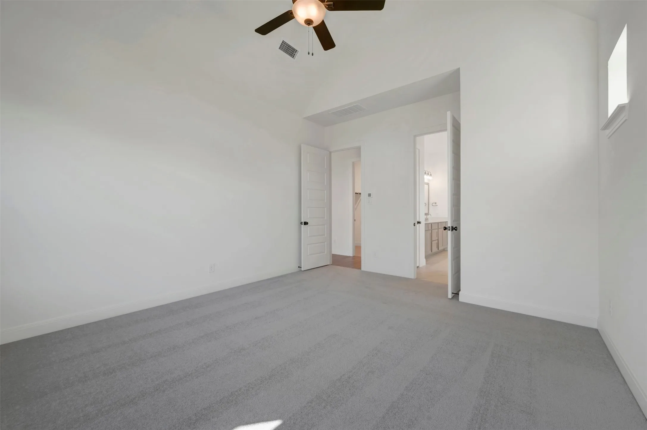 Vaulted ceiling with an attached ceiling fan, light gray carpeting, and a window