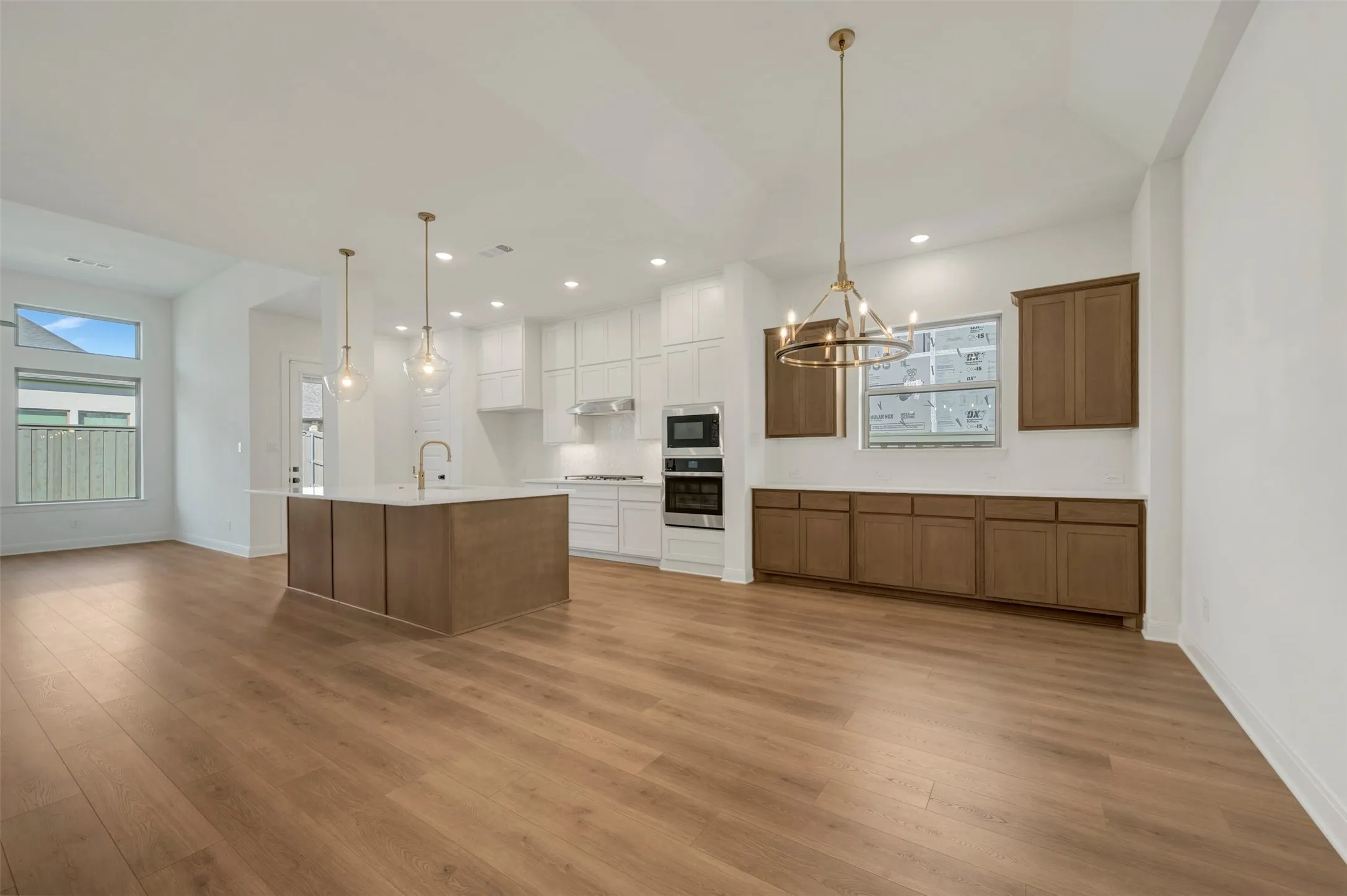 Open-concept living space with wood-finish flooring, vaulted ceilings, and a kitchen island featuring a gold-finish faucet