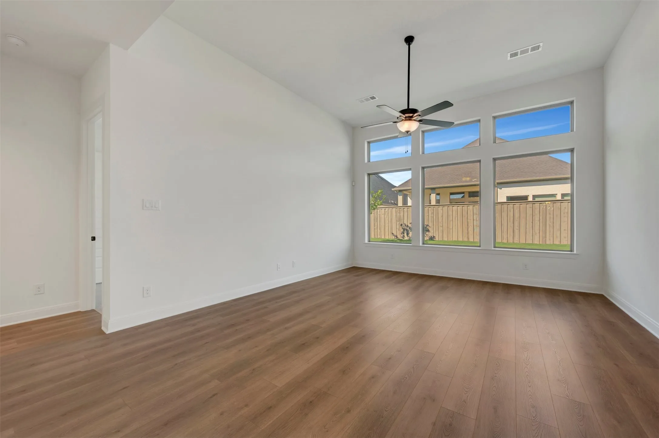 Spacious room featuring wood-finish flooring, a contemporary ceiling fan, and a wall of windows