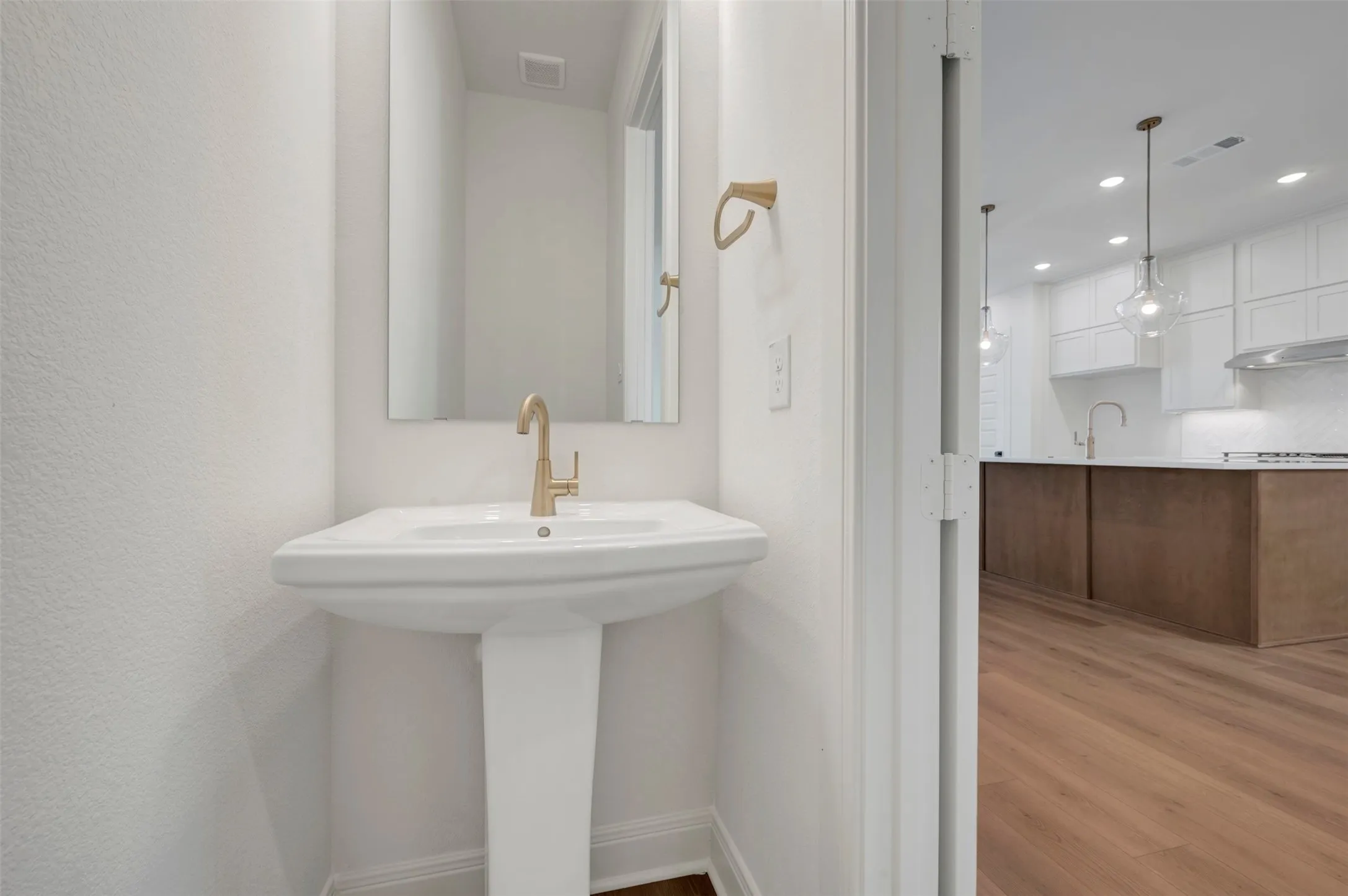 Pedestal sink with brass-finish faucet, wall-mounted mirror, and wood-finish flooring