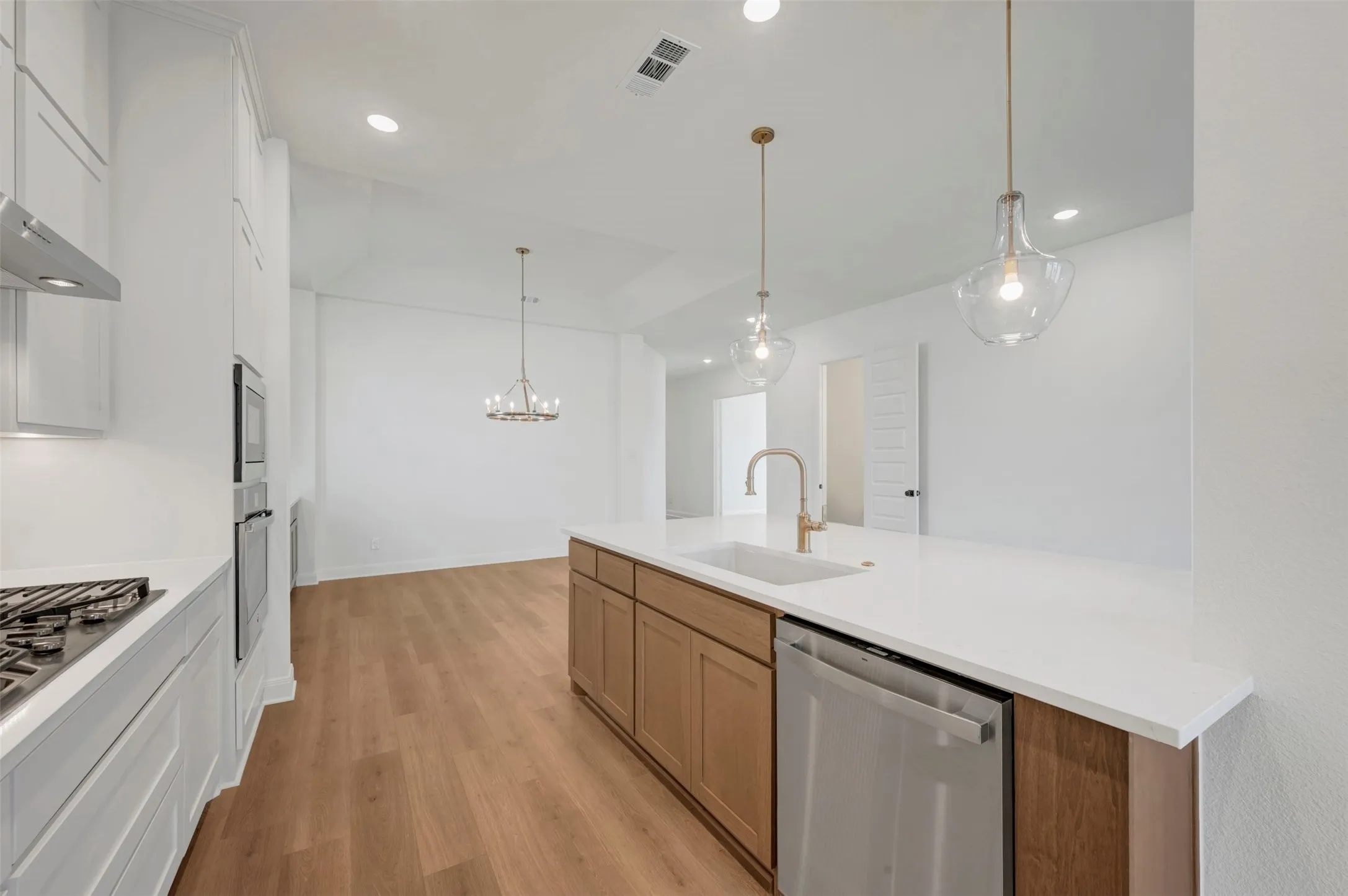 Kitchen featuring a large central island with an undermount sink, stainless steel dishwasher, and two pendant lights