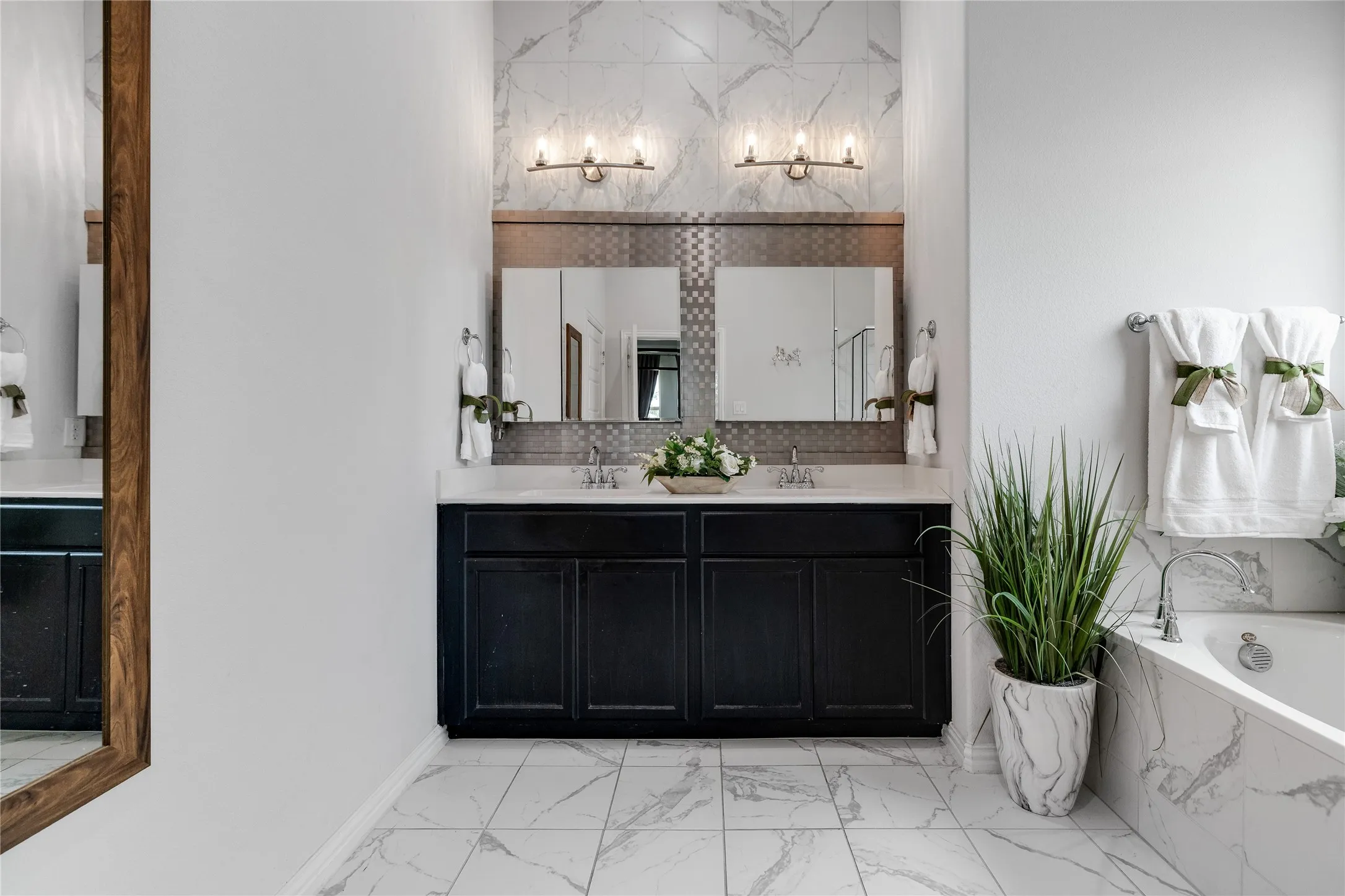 Dual vanity with dark cabinetry and white countertops, complemented by large format tile flooring and a built-in soaking tub