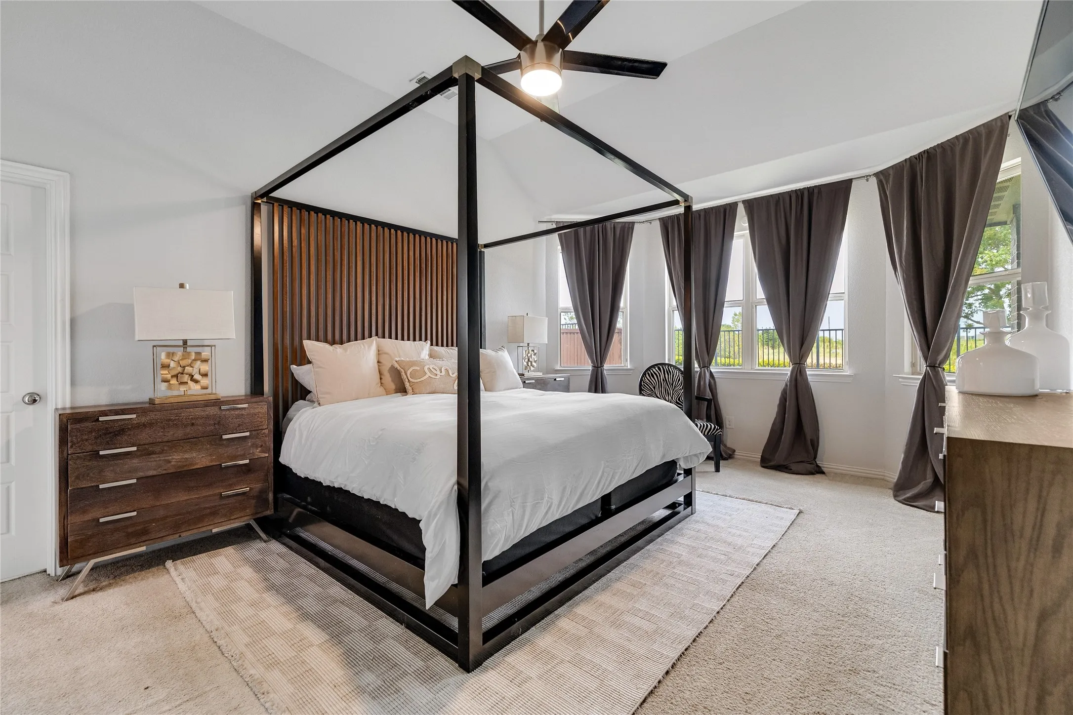 Vaulted ceiling with a ceiling fan, multiple windows with roller shades, and light-toned carpeting