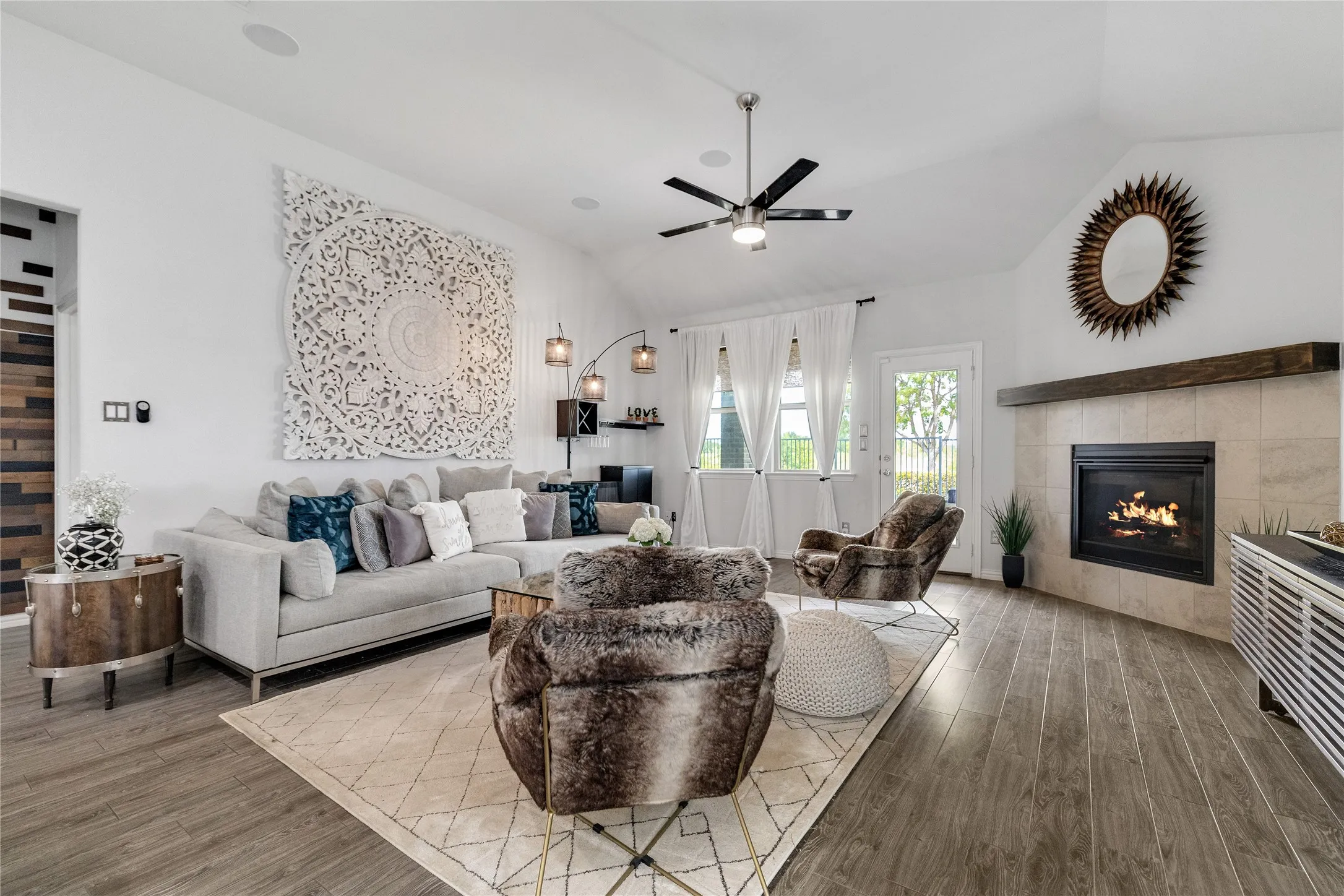 Vaulted ceilings, wood-finish flooring, a contemporary ceiling fan, and a tiled fireplace with a wood mantle