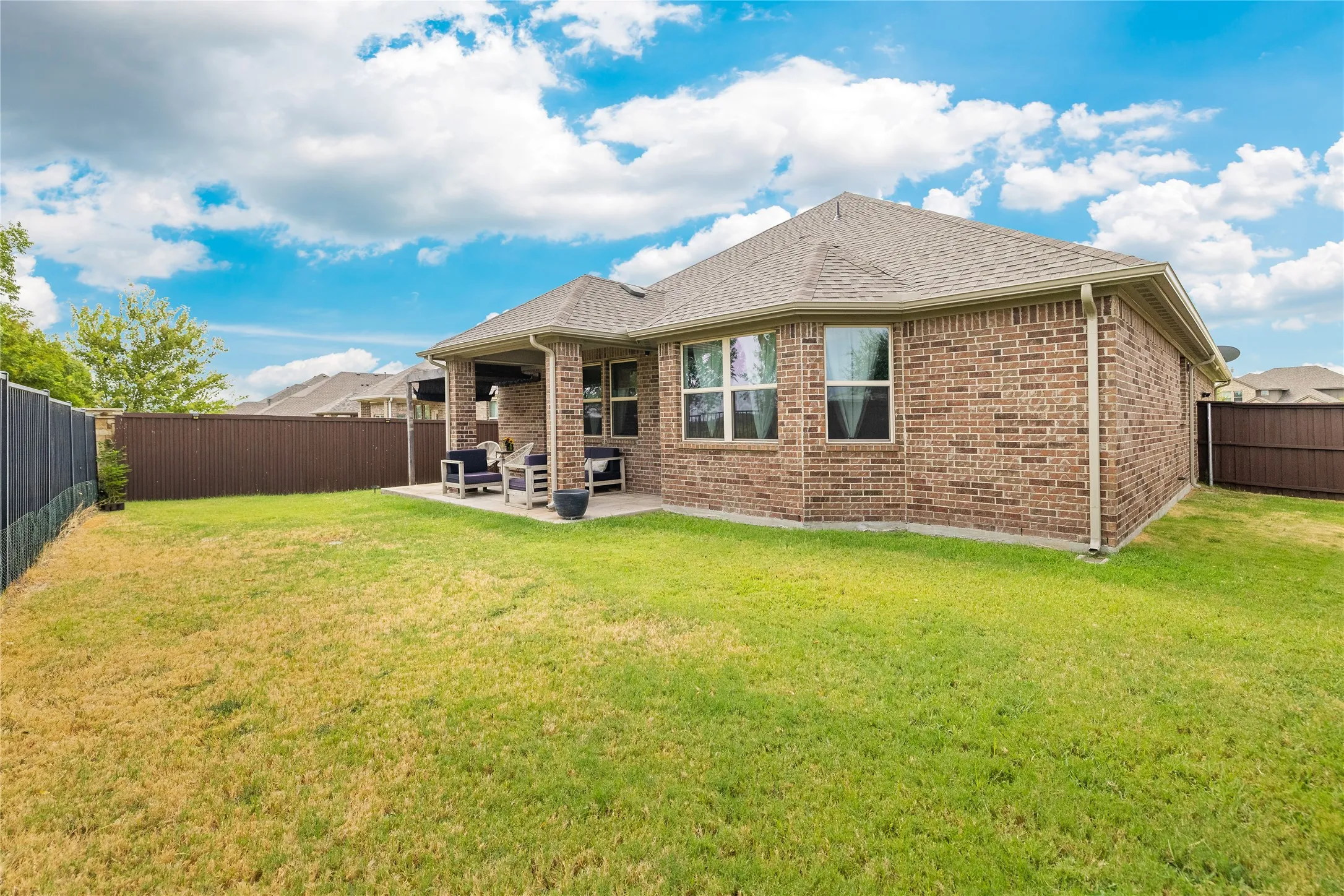 Brick exterior with a covered patio, multiple windows, and a fenced backyard