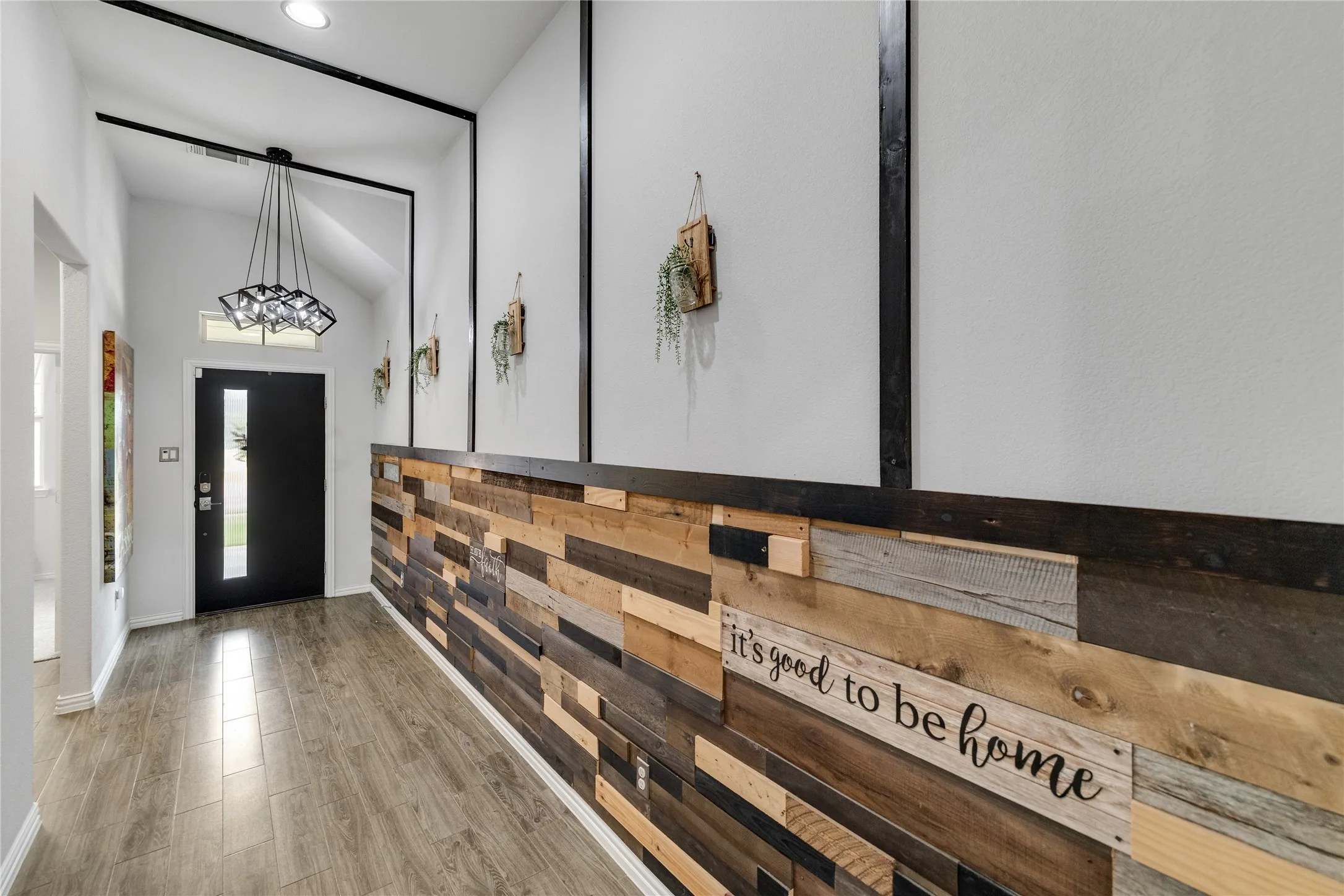 Vaulted entry featuring a decorative light fixture, wood-finish flooring, and a decorative accent wall