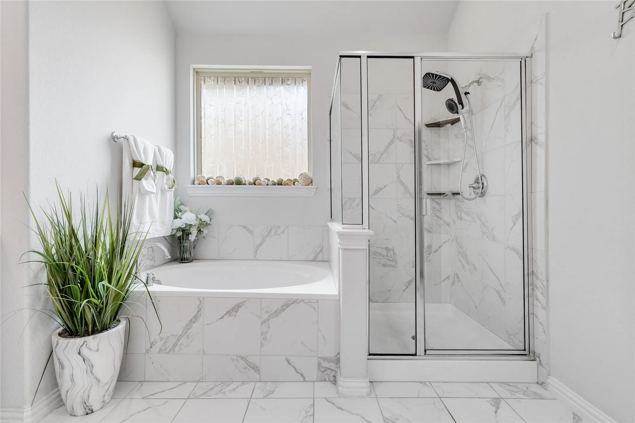 Freestanding soaking tub with marble-patterned tile surround, glass-enclosed shower with marble-patterned tile, and chrome fixtures