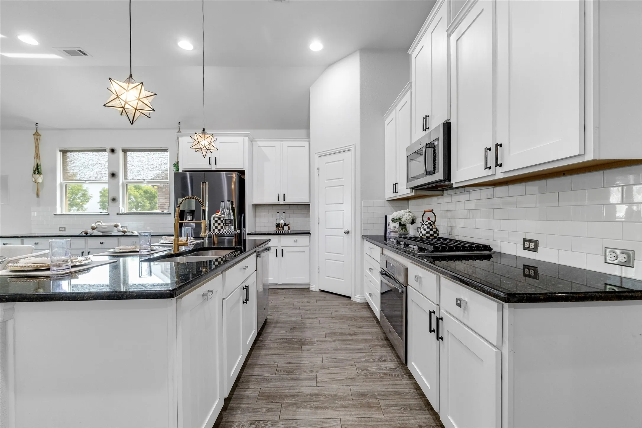 White shaker cabinetry, dark countertops, a subway tile backsplash, and wood-finish flooring