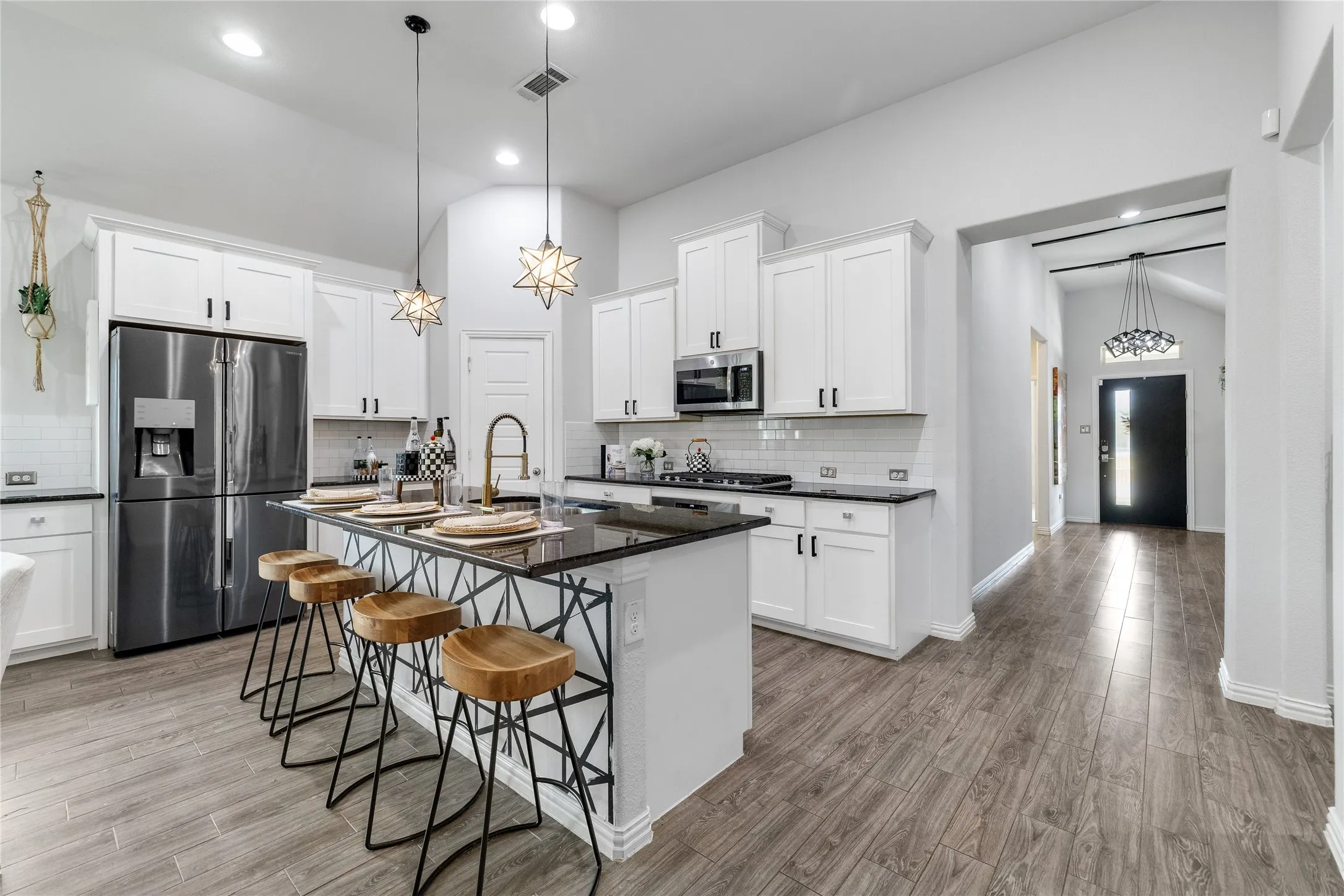 Kitchen with white shaker cabinetry, black countertops, stainless steel appliances, and wood-finish flooring