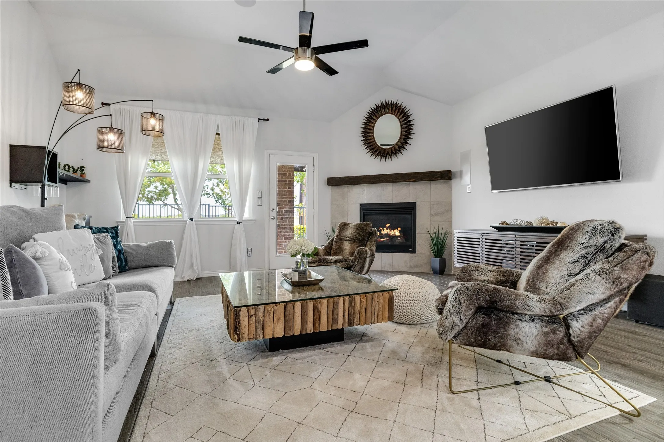 Vaulted ceiling with a ceiling fan, fireplace with a wood mantel, light wood-finish flooring, and a glass-paneled exterior door