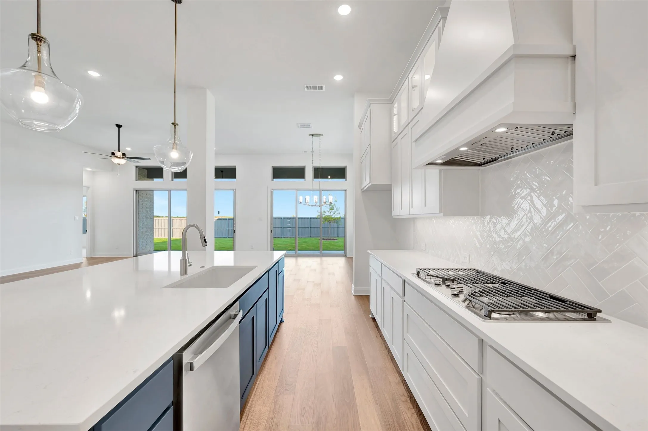 Kitchen featuring a gas cooktop, herringbone tile backsplash, white countertops, wood-finish flooring, and pendant lighting