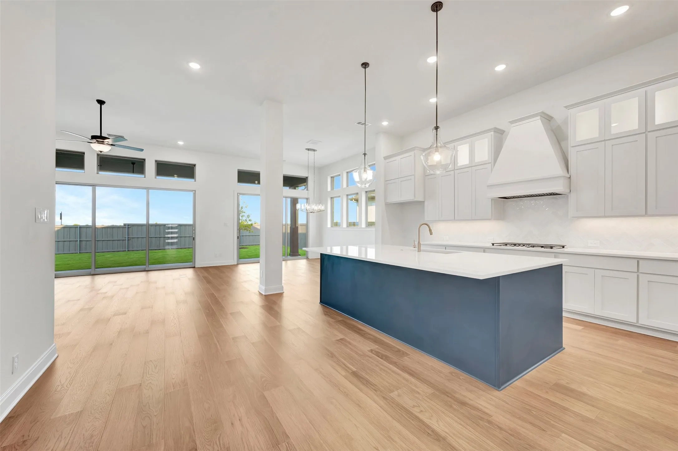 Open-concept living space with wood-finish flooring, a contemporary kitchen island, white cabinetry, and sliding glass doors to the backyard
