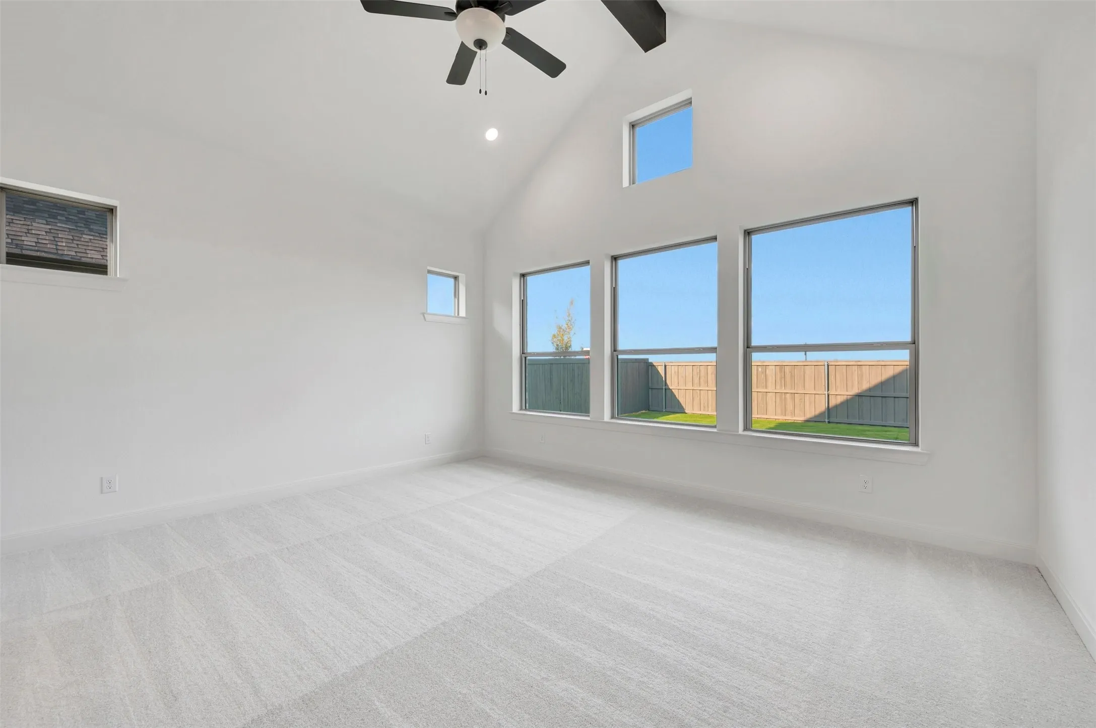 Vaulted ceiling with integrated ceiling fan, multiple transom windows, expansive windows, and light-toned carpeting