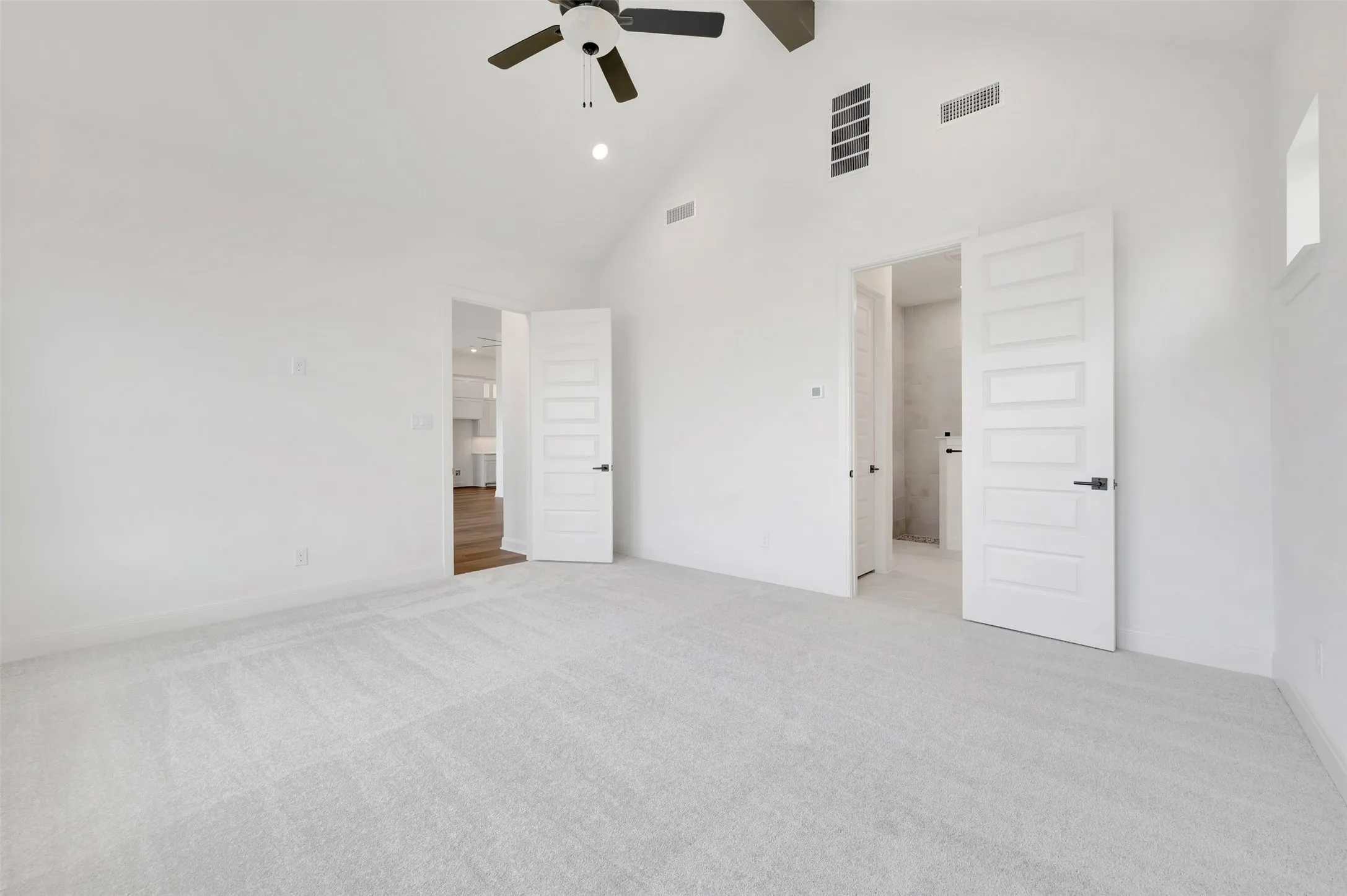 Vaulted ceiling with an exposed beam, light-colored carpeting, modern panel doors, and a ceiling fan with integrated lighting