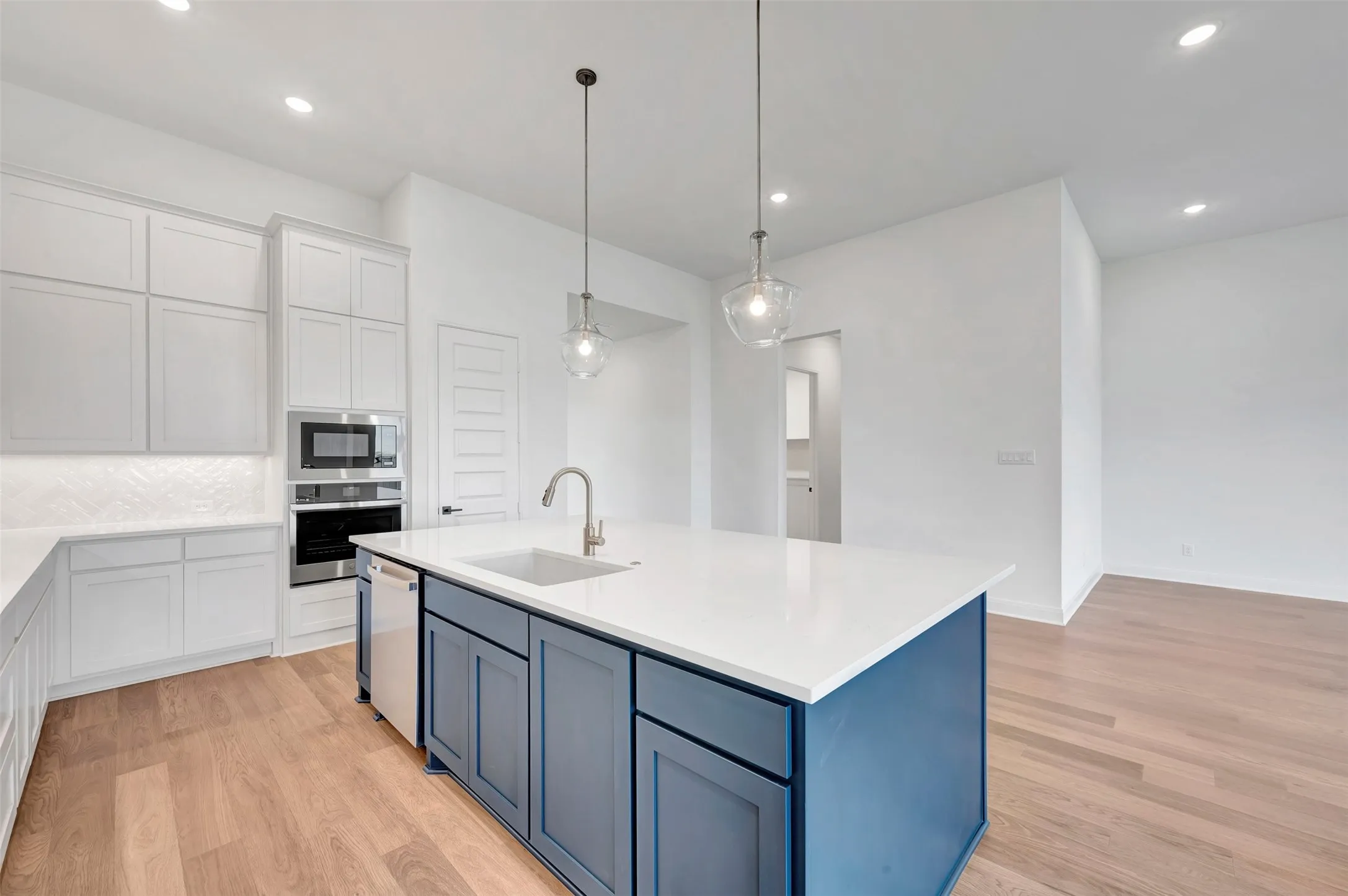 Wood-finish flooring, white cabinetry, built-in stainless steel appliances, blue center island with integrated sink, and pendant lighting