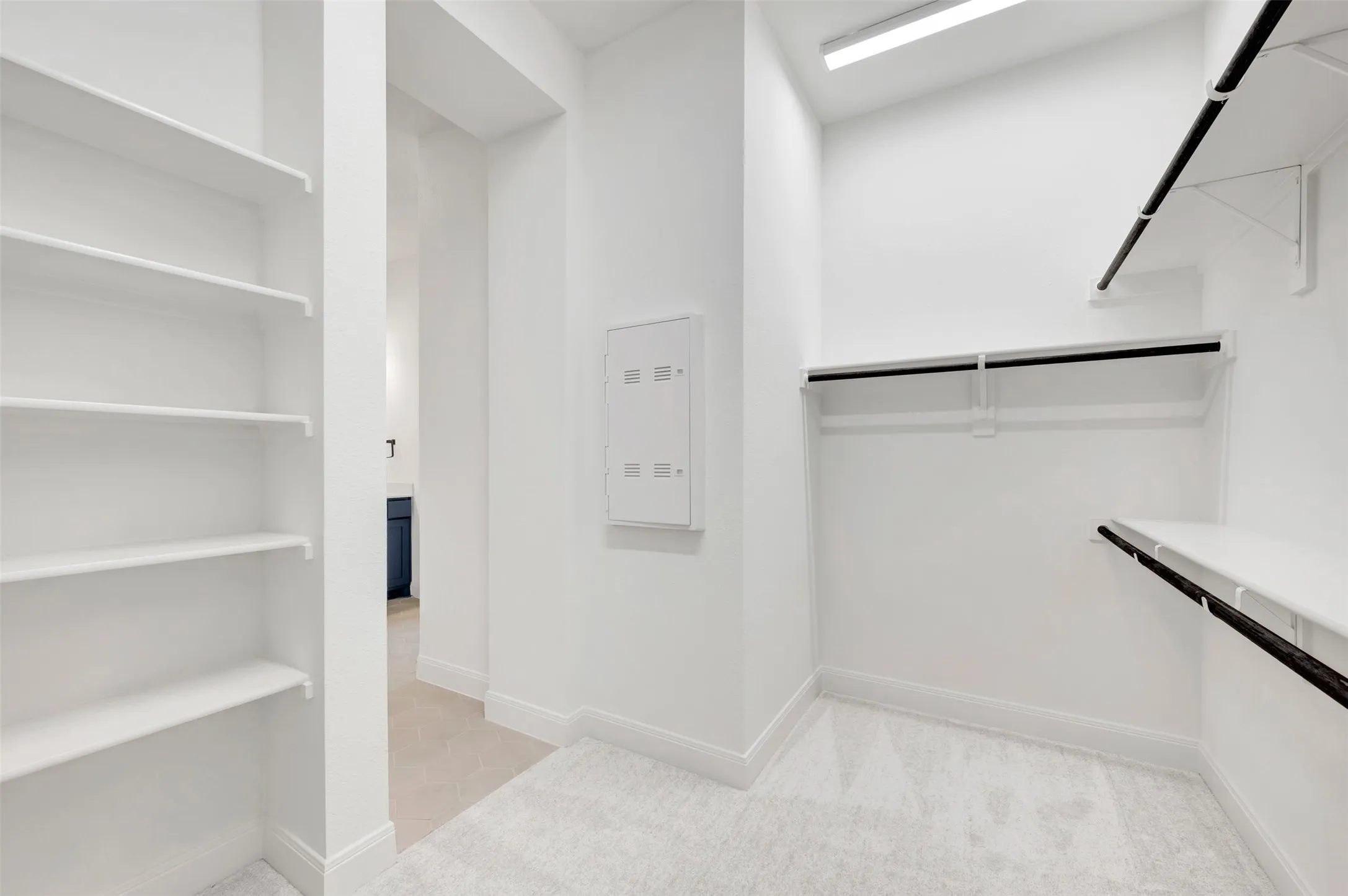 Spacious walk-in closet featuring extensive built-in shelving, dual clothing rods with black metal hardware, light-finish flooring, and bright recessed lighting throughout