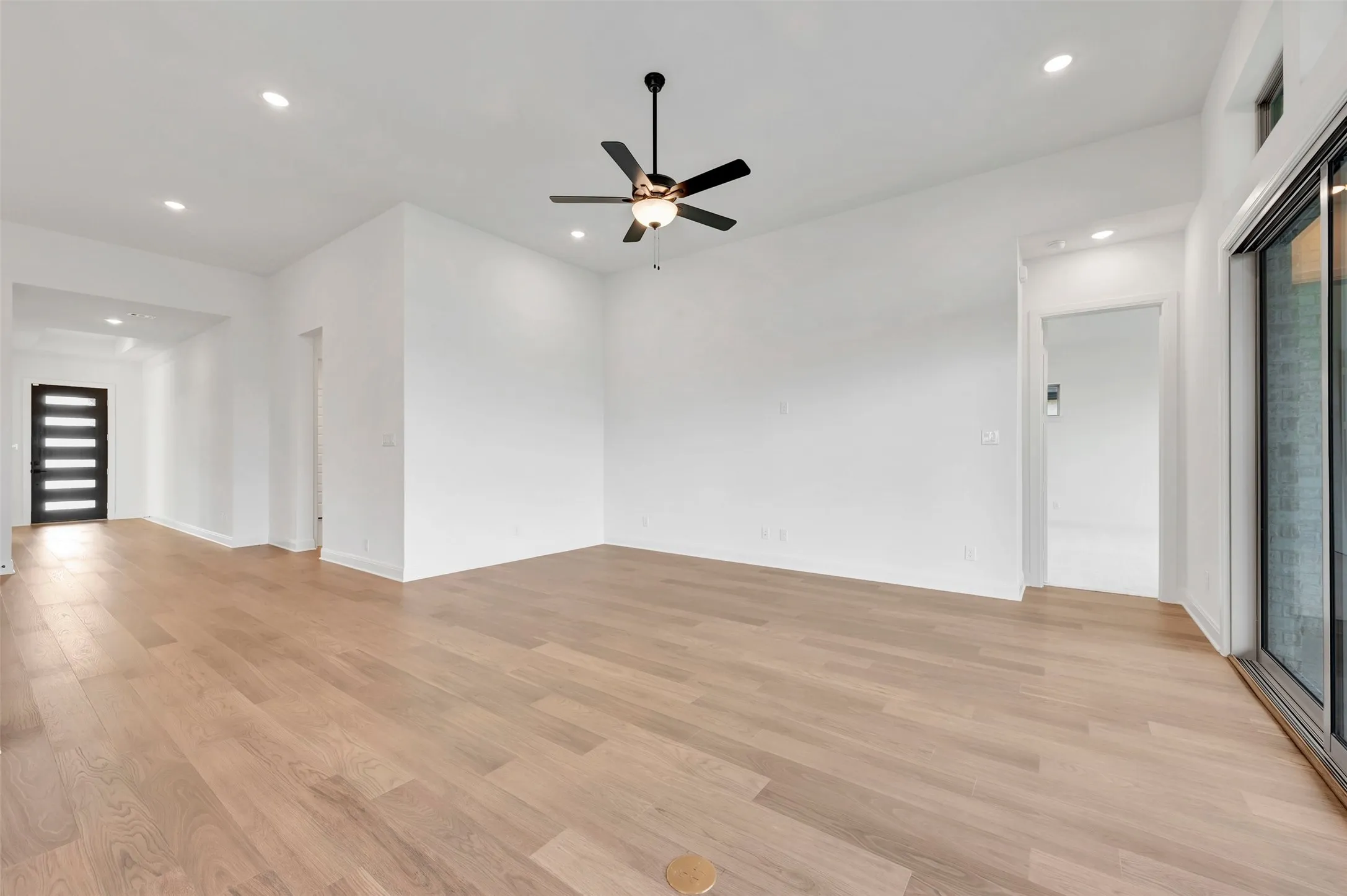 Wood-finish flooring, recessed lighting, ceiling fan with light, modern entry door with frosted glass panels, and sliding glass patio door