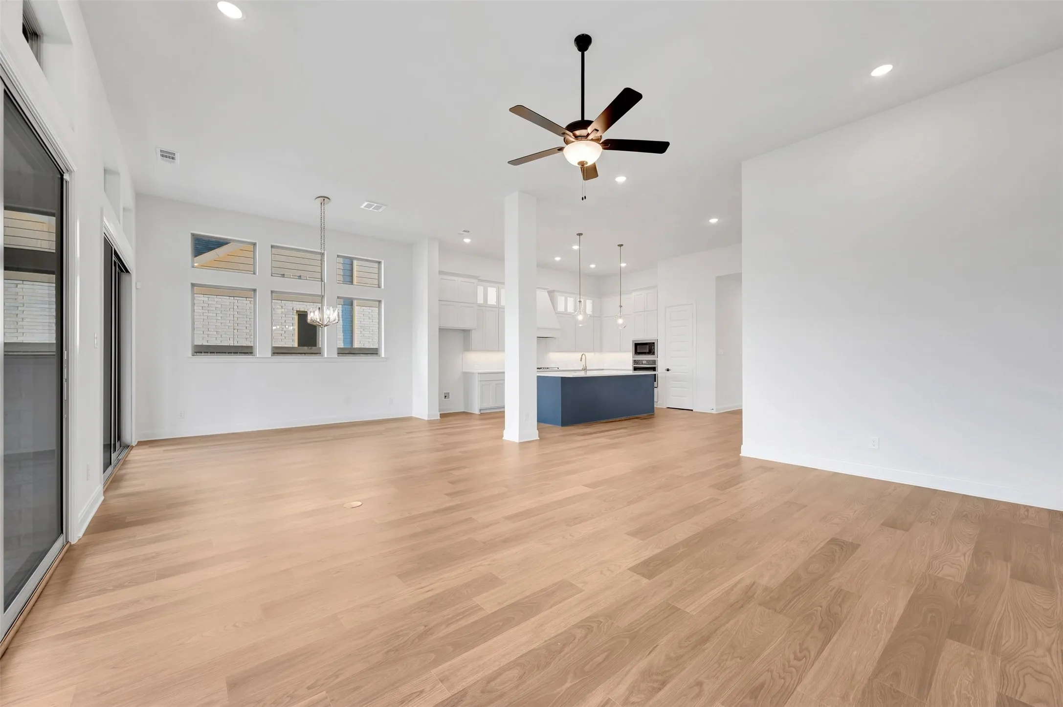 Recessed lighting, wood-finish flooring, ceiling fan, sliding glass doors, and a kitchen island with pendant lighting