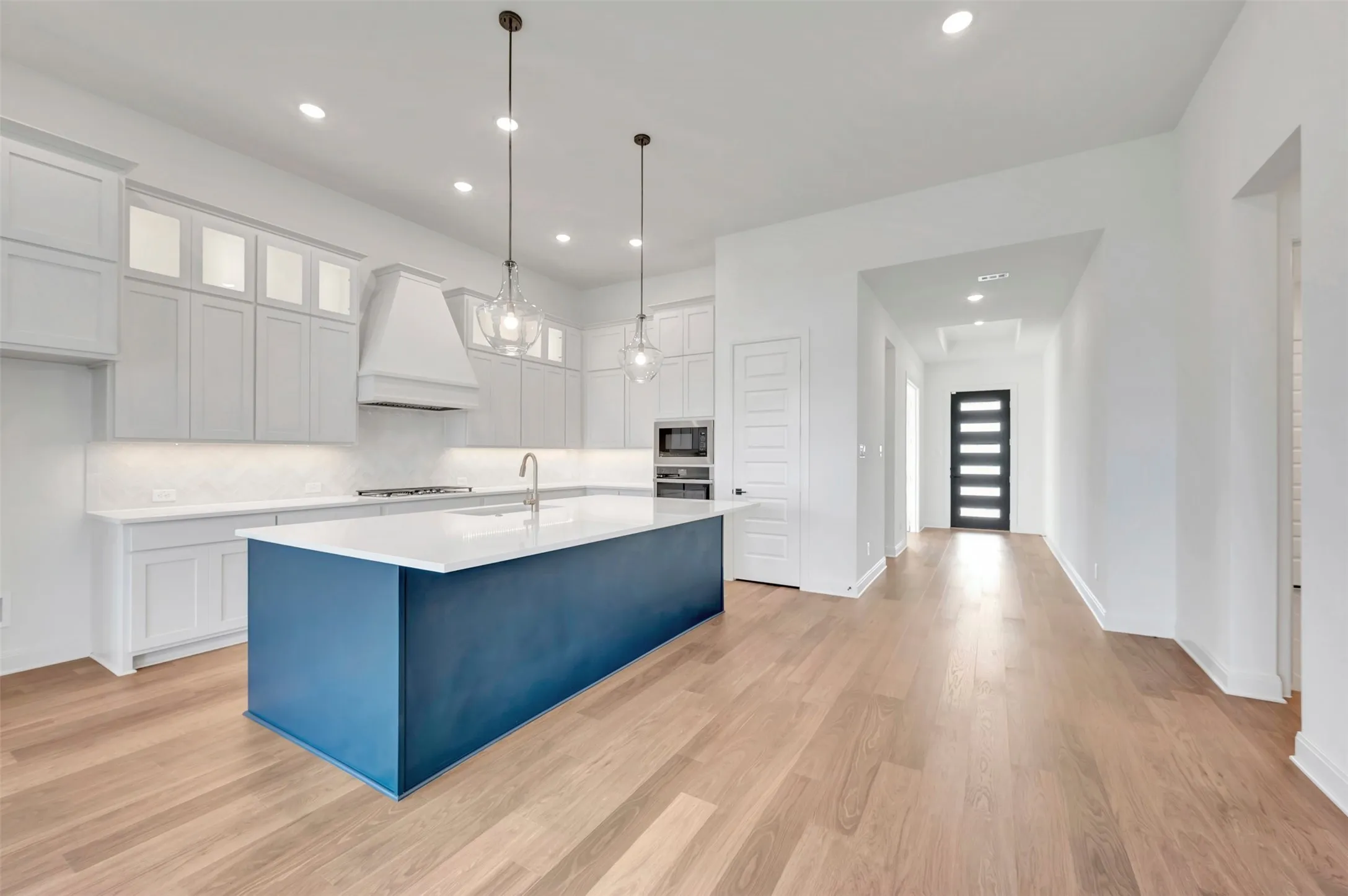 Gourmet kitchen with a contrasting blue island, white shaker cabinetry, stainless steel appliances, and wood-finish flooring