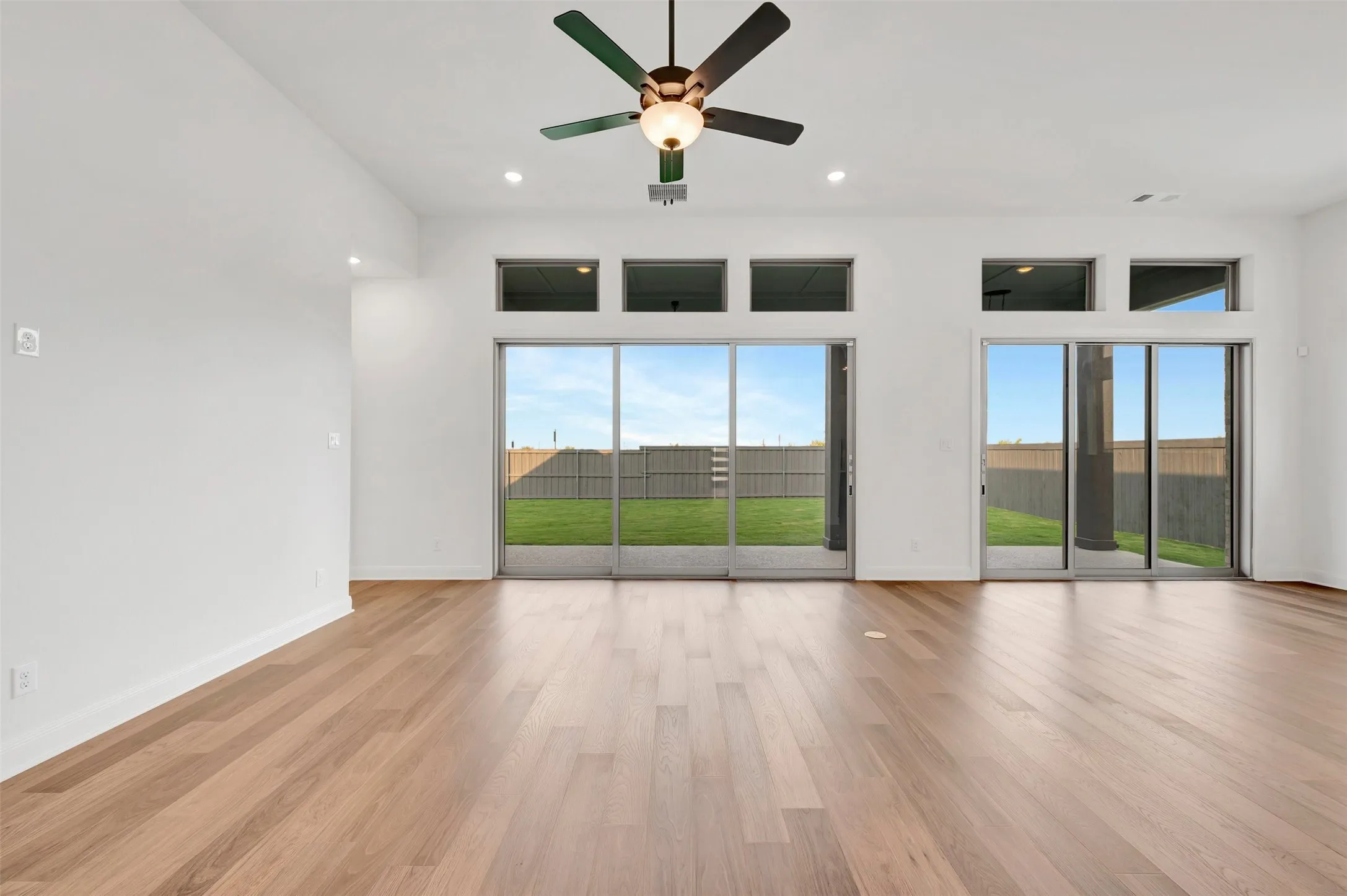 Wide plank wood-finish flooring, recessed lighting, ceiling fan light fixture, sliding glass doors, and a manicured lawn