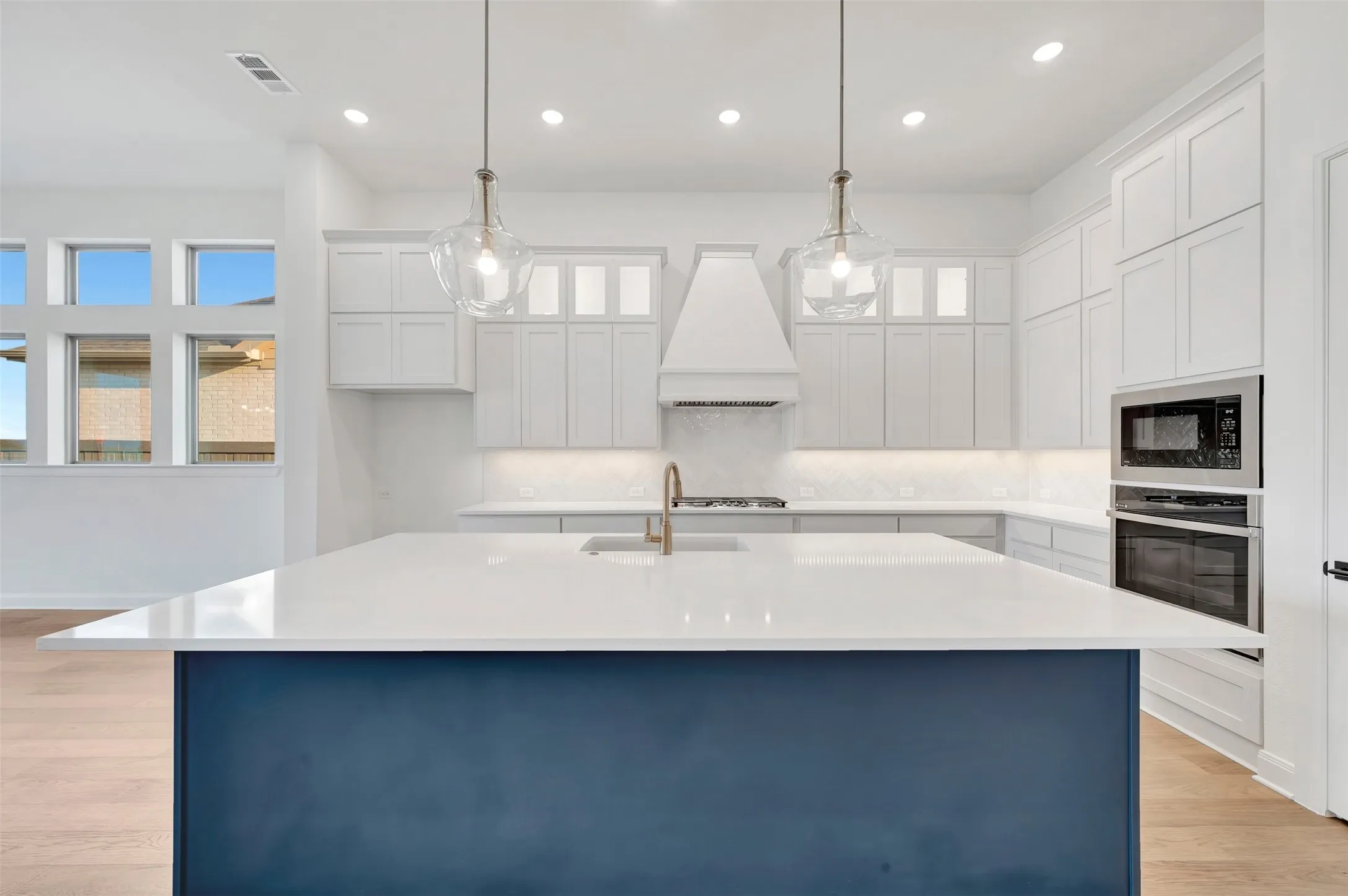 Kitchen featuring a blue-toned island, light-toned countertops, white cabinetry, built-in stainless steel appliances, and pendant lighting