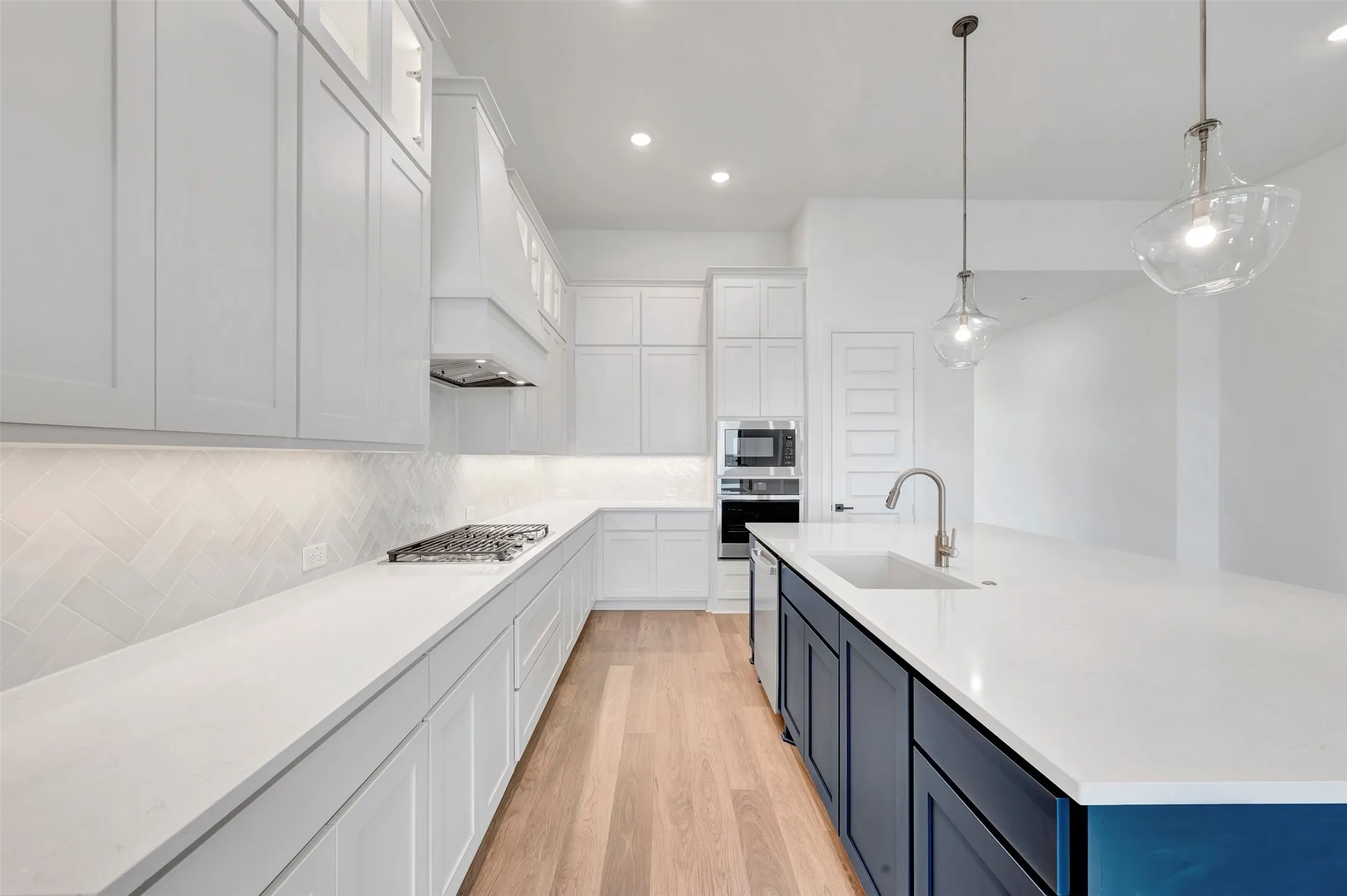 Modern kitchen featuring white shaker cabinetry, white countertops, stainless steel appliances, wood-finish flooring, and a blue island with a built-in sink